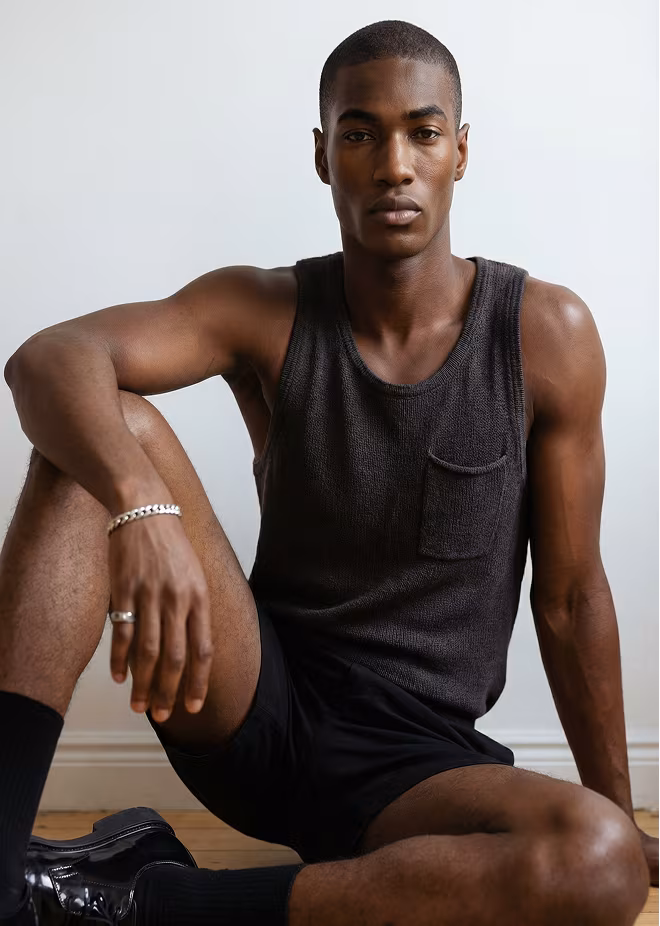 A black and white image of Botika's black male AI fashion model in side profile wearing a black suite jacket and white collared shirt.