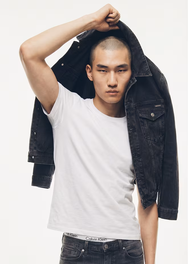 Botika Asian male fashion model Kazuto wearing a white tshirt and black dress pants standing on the roof of a building with the city behind him.