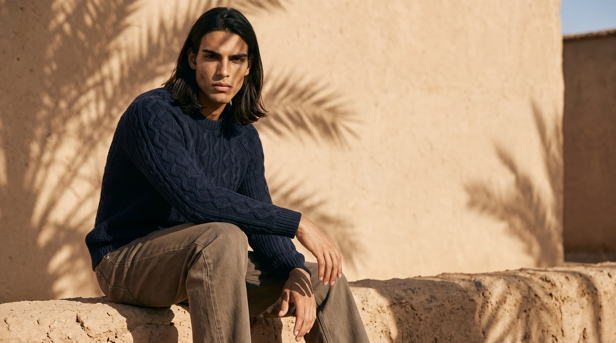 Man seated on a stone step in a navy cable-knit sweater and tan trousers, AI on-model image