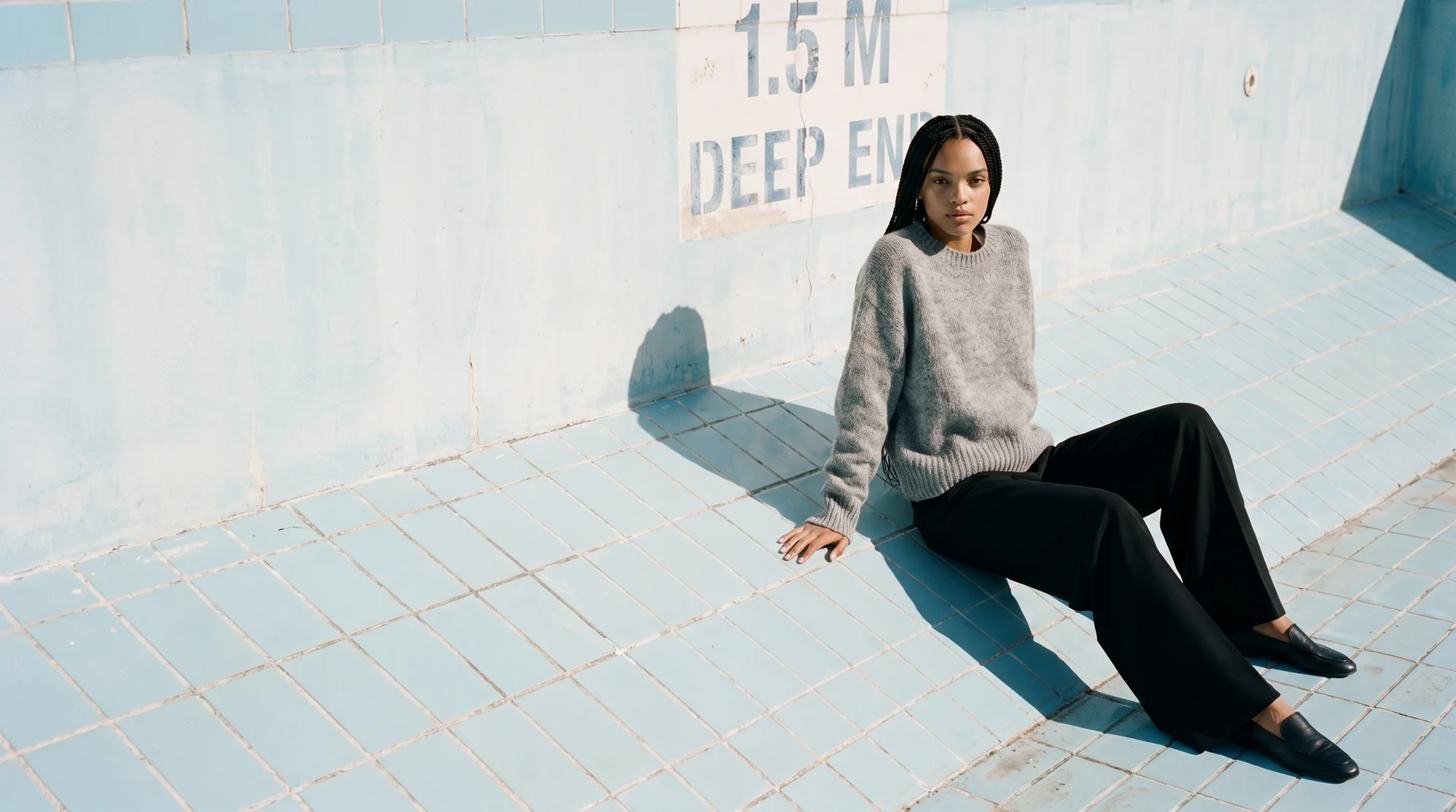 Woman seated on a white studio floor in a grey mohair sweater and black trousers, AI on-model image
