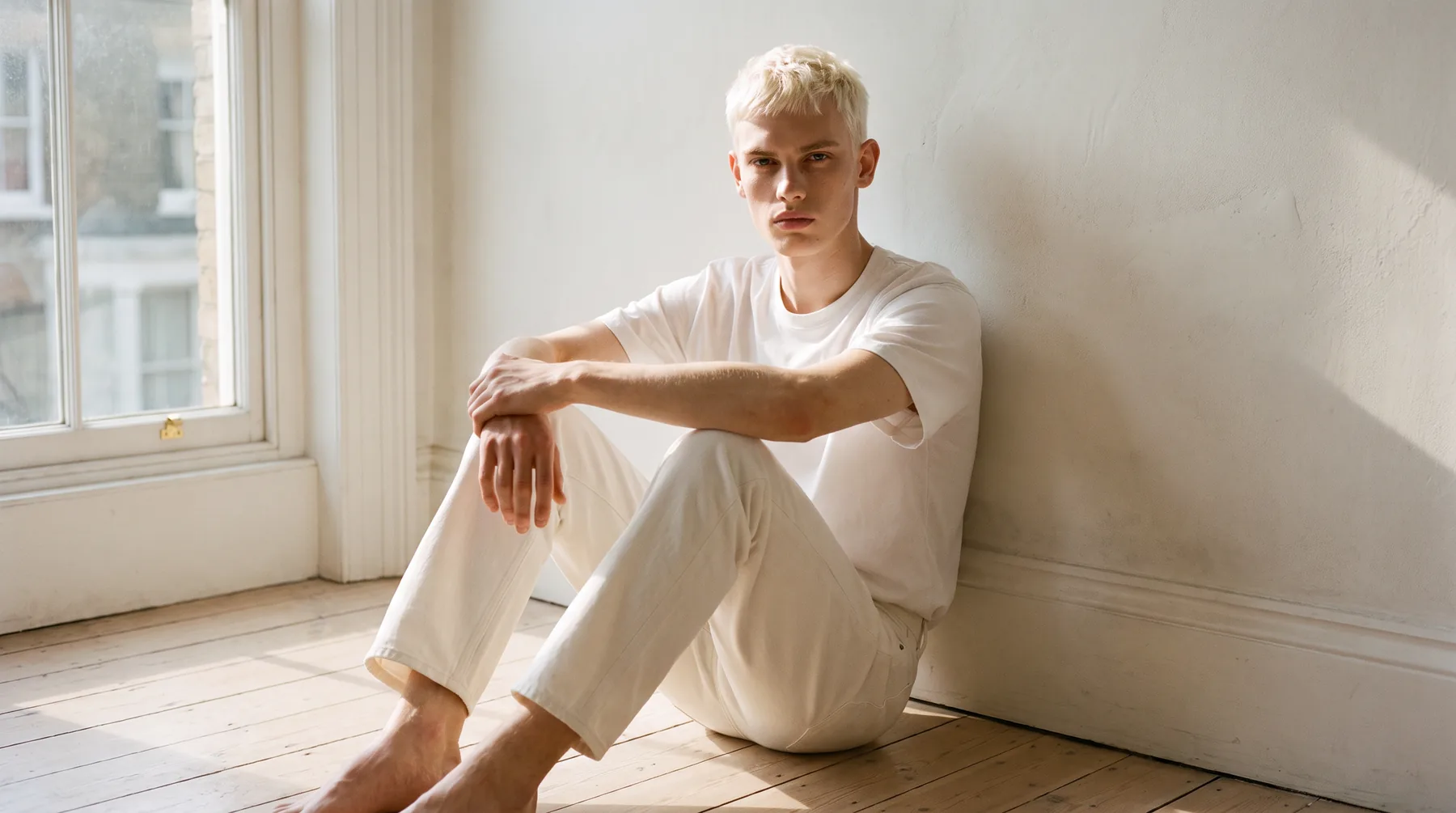 Man seated by a window in a white t-shirt and cream jeans, AI-generated on-model image