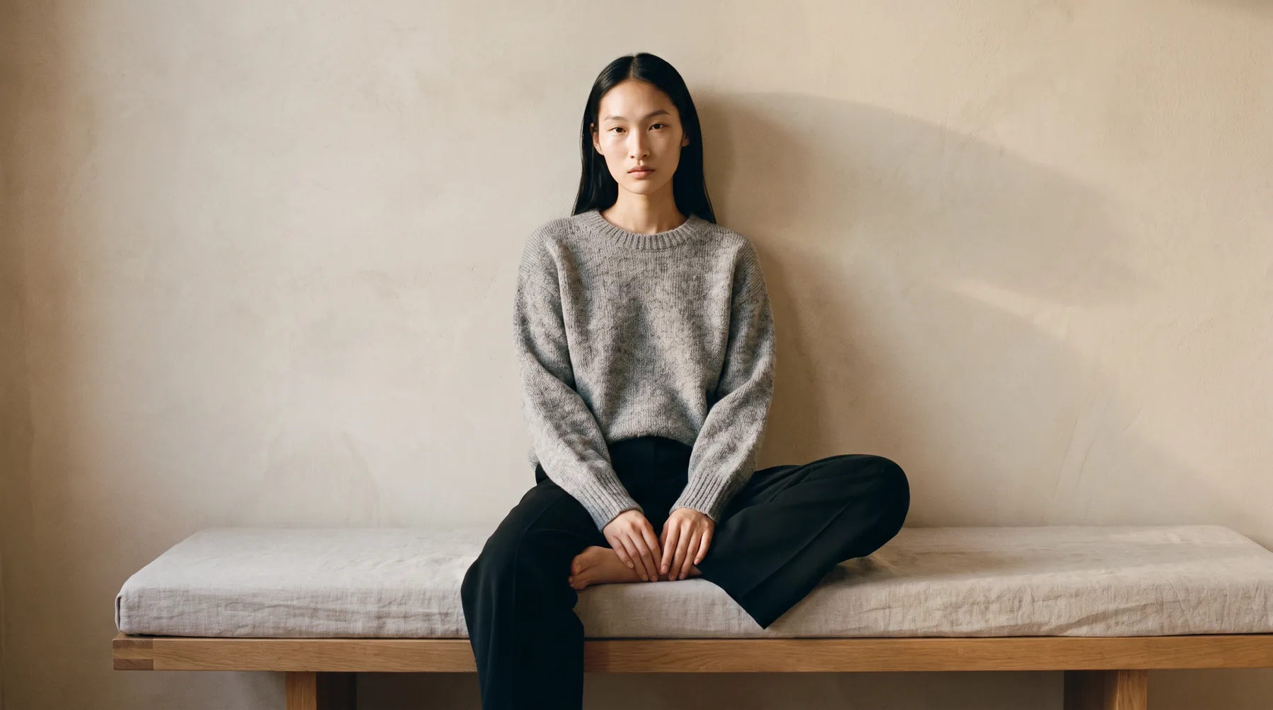 Woman seated on a bench against a chalk plaster wall in a mohair sweater, AI on-model image