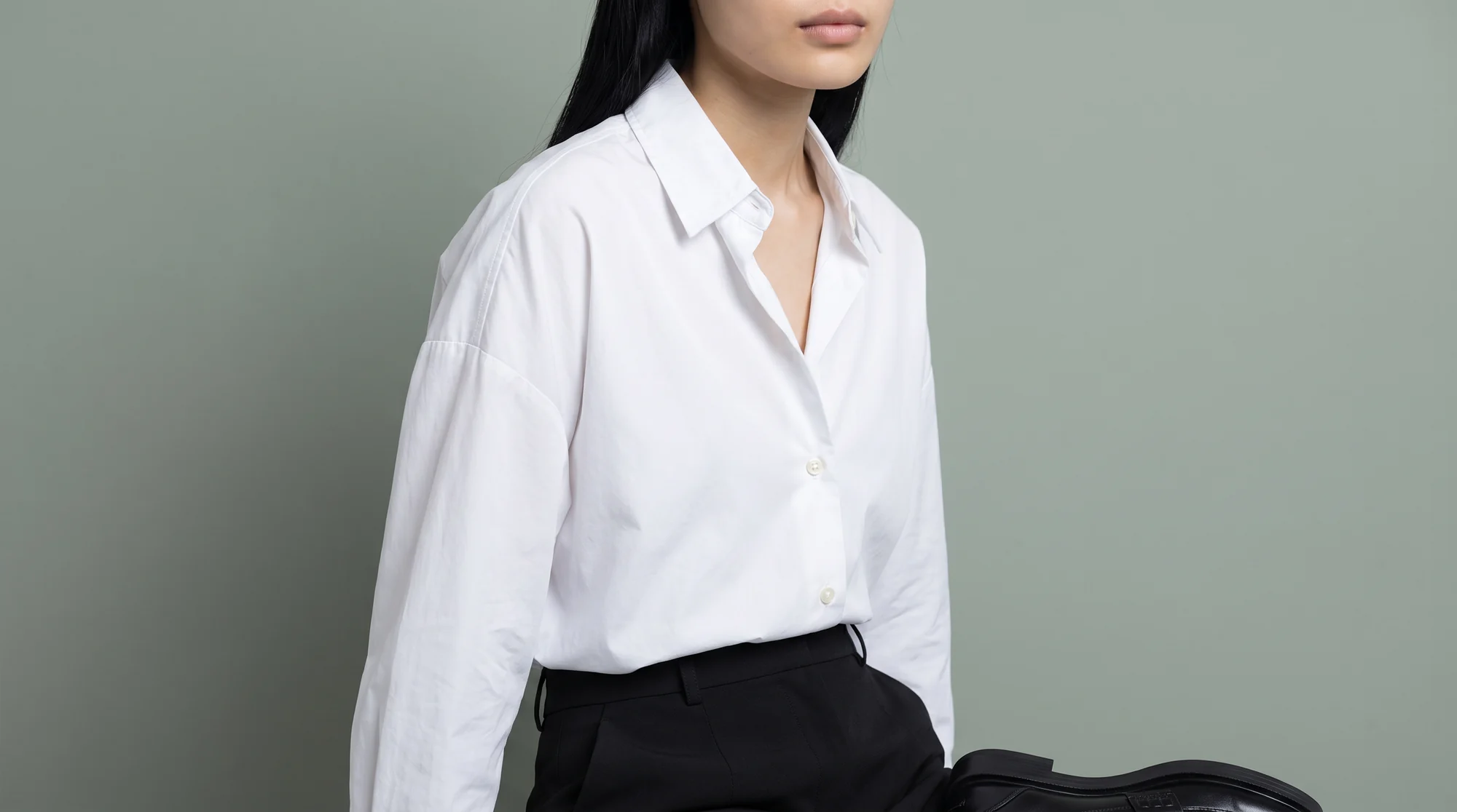 Tight crop on a crisp white shirt collar and shoulder against a muted sage background