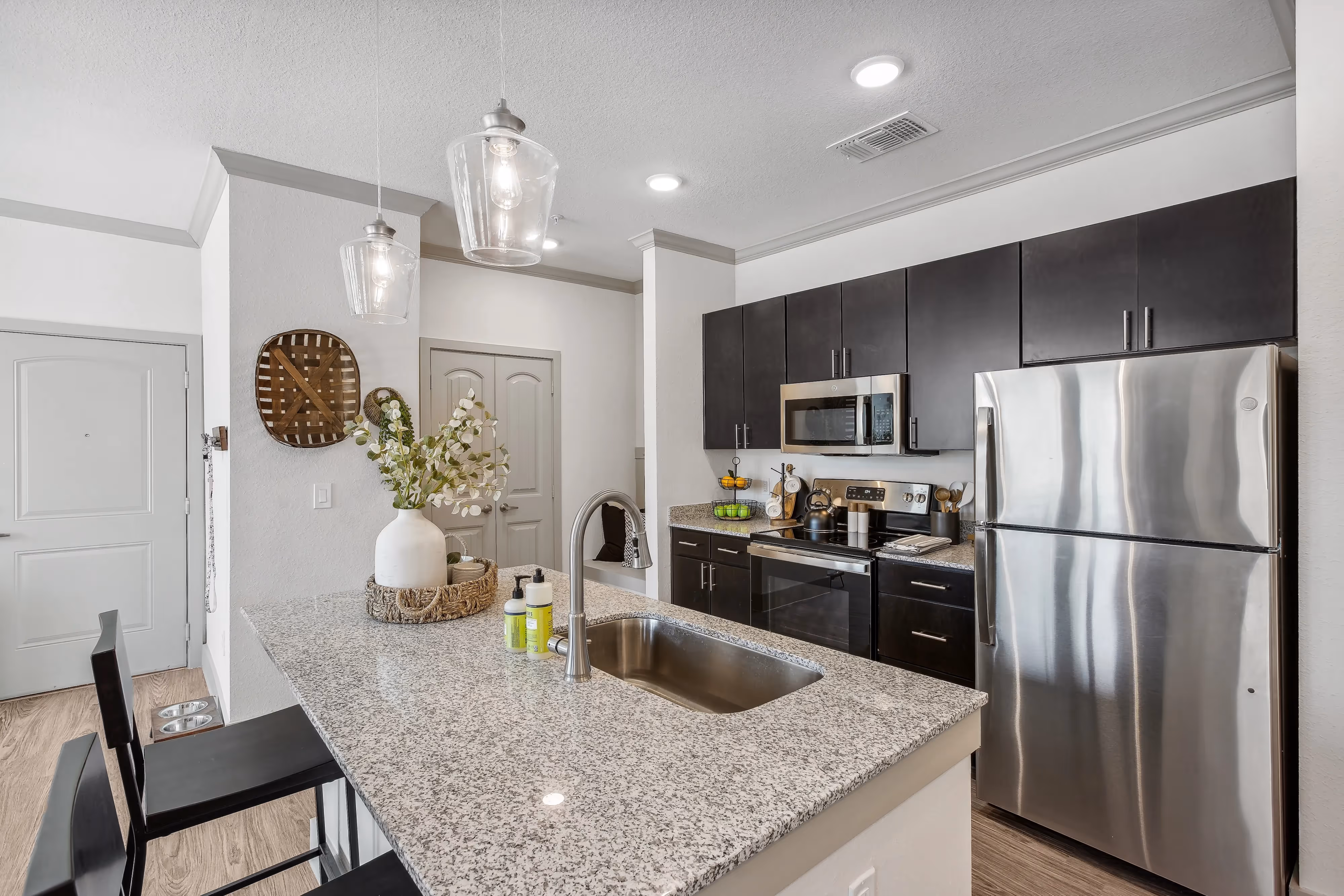 Apartment kitchen with a large granite-top island with a sink and seating, and dark cabinetry, at Paloma Luxury Apartments in San Antonio, TX.