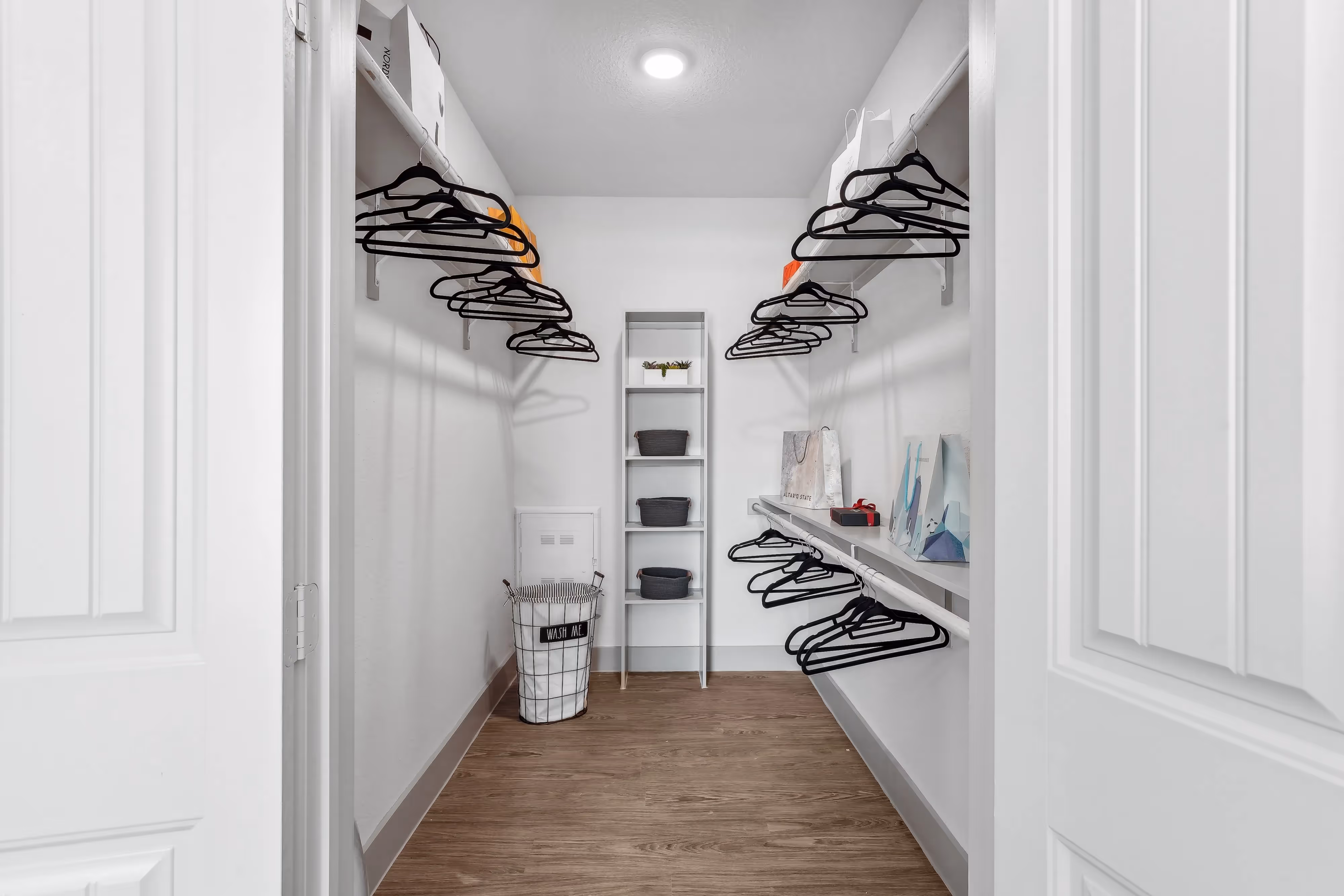 Walk-in closet with ample shelving, a central organizer, and wood-style flooring in an apartment at Paloma Luxury Apartments in San Antonio, TX.