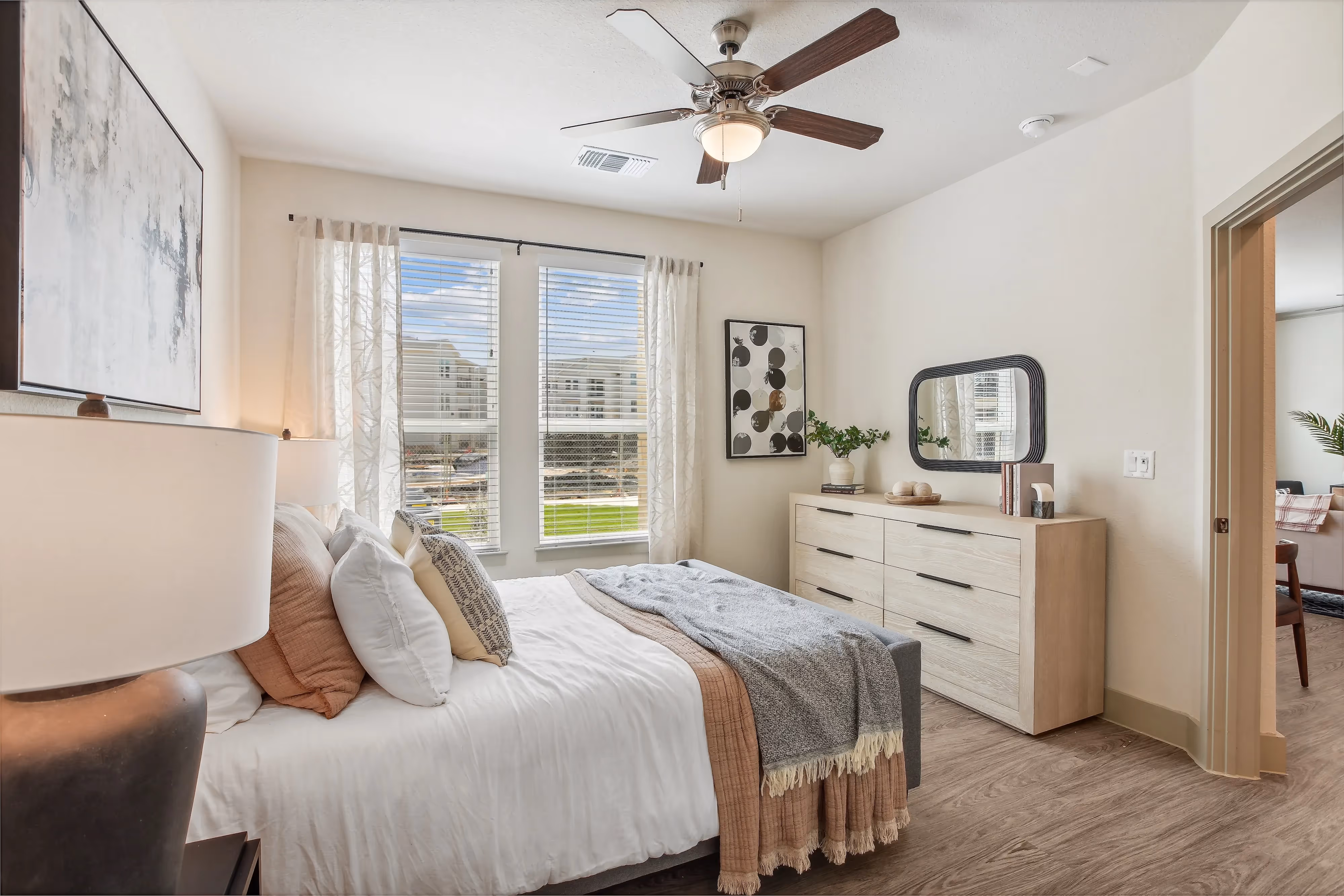Bright bedroom with a large window, ceiling fan, and wood-style flooring, showcasing an apartment at Paloma Luxury Apartments in San Antonio, TX.