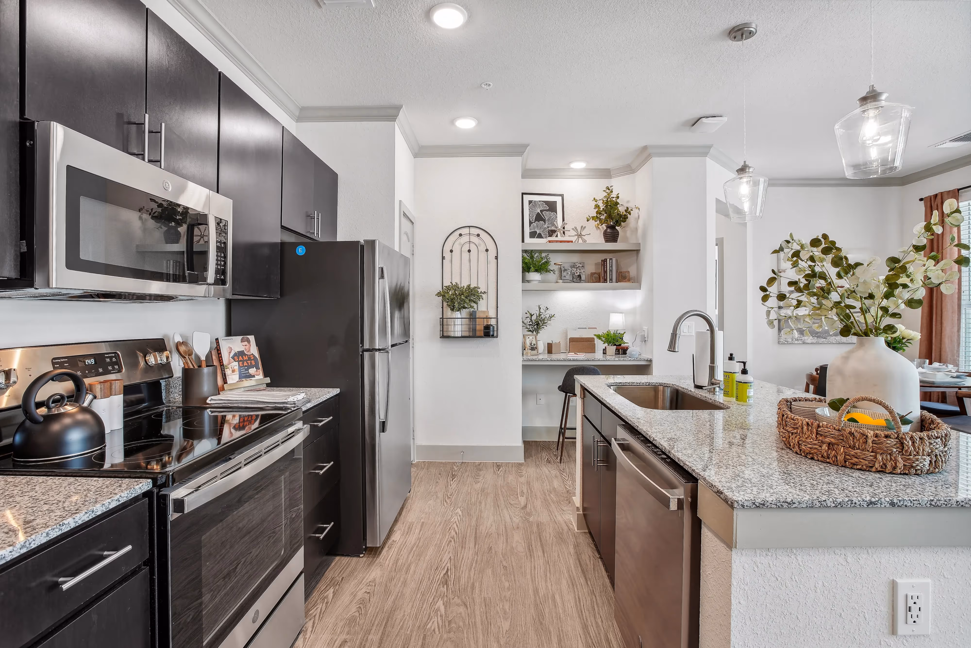 Modern kitchen with dark cabinets, granite countertops, and a unique kitchen bar with shelving, at Paloma Luxury Apartments in San Antonio, TX.