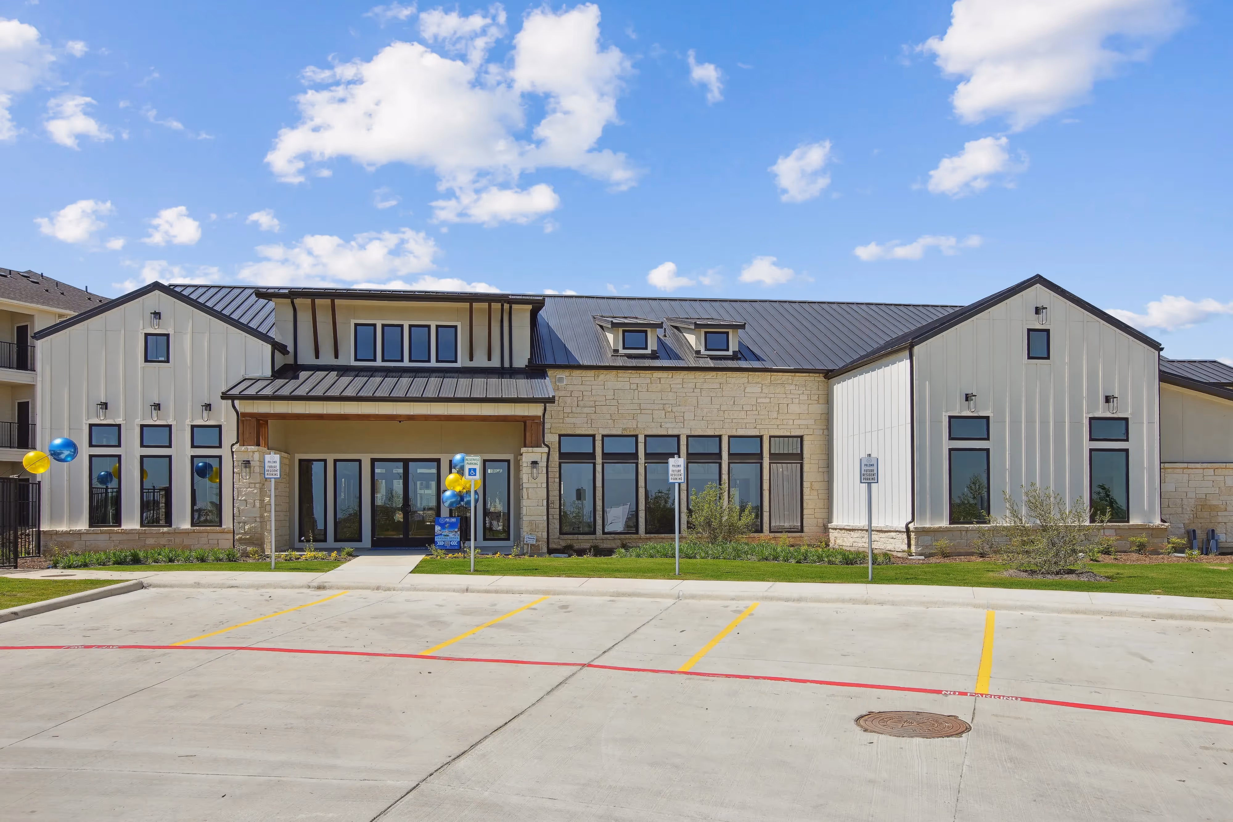 Exterior of the modern farmhouse-style clubhouse or leasing office with stone and white siding, at Paloma Luxury Apartments in San Antonio, TX.