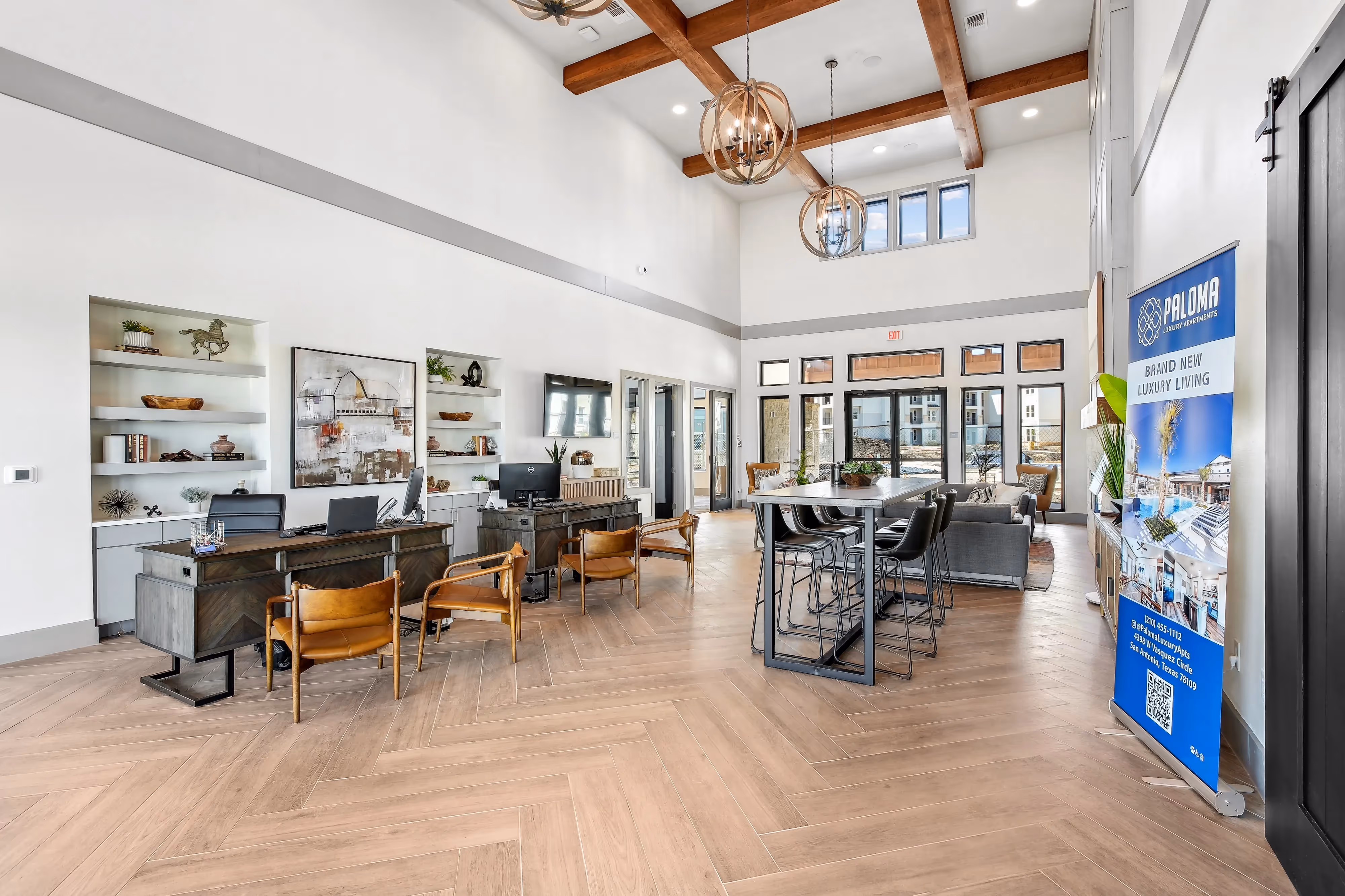 Elegant clubhouse with a co-working space, high-top tables, and lounge seating, with a "Brand New Luxury Living" banner visible, at Paloma Luxury Apartments in San Antonio, TX.