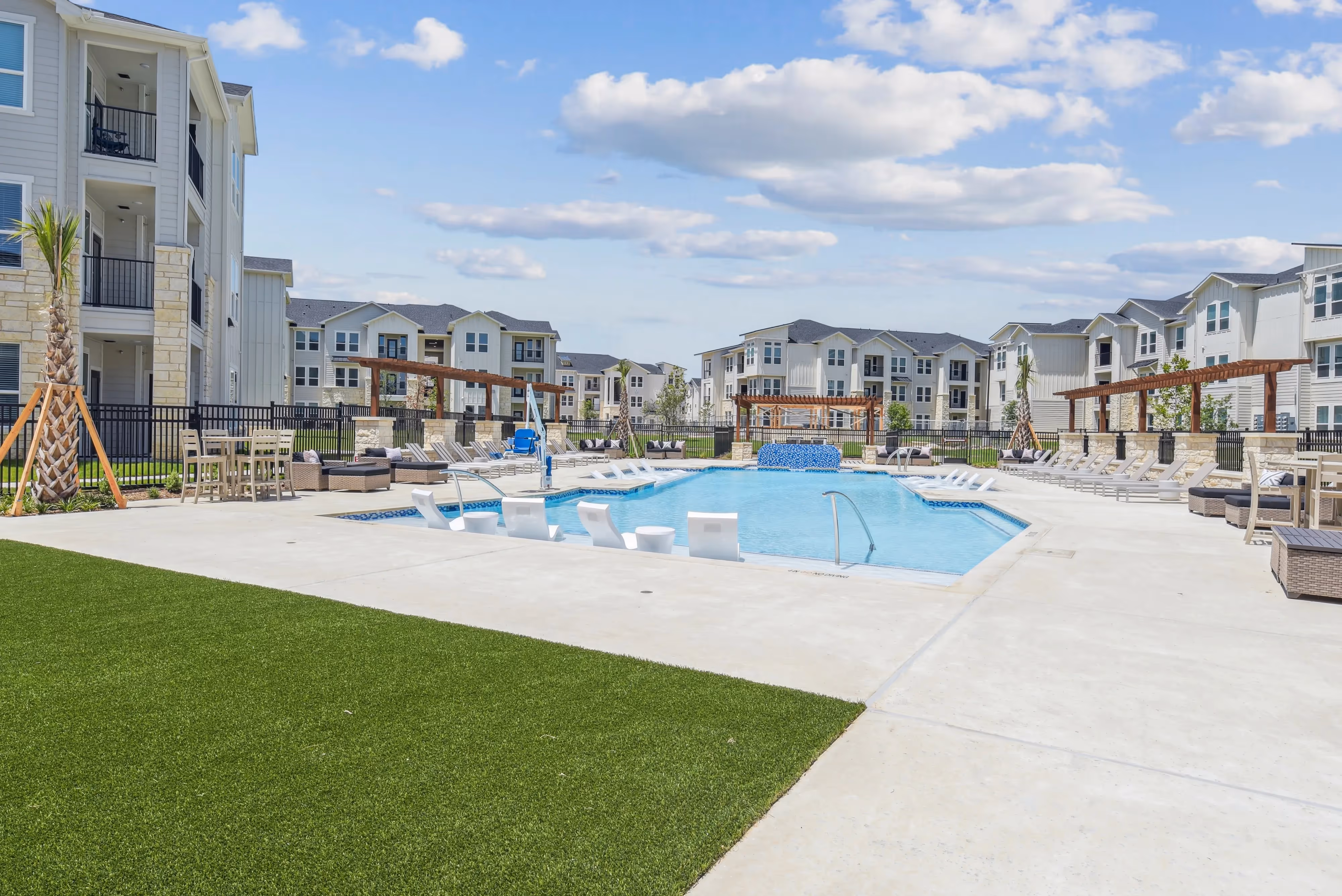 Central swimming pool area with built-in lounge chairs and surrounded by modern residential buildings at Paloma Luxury Apartments in San Antonio, TX.