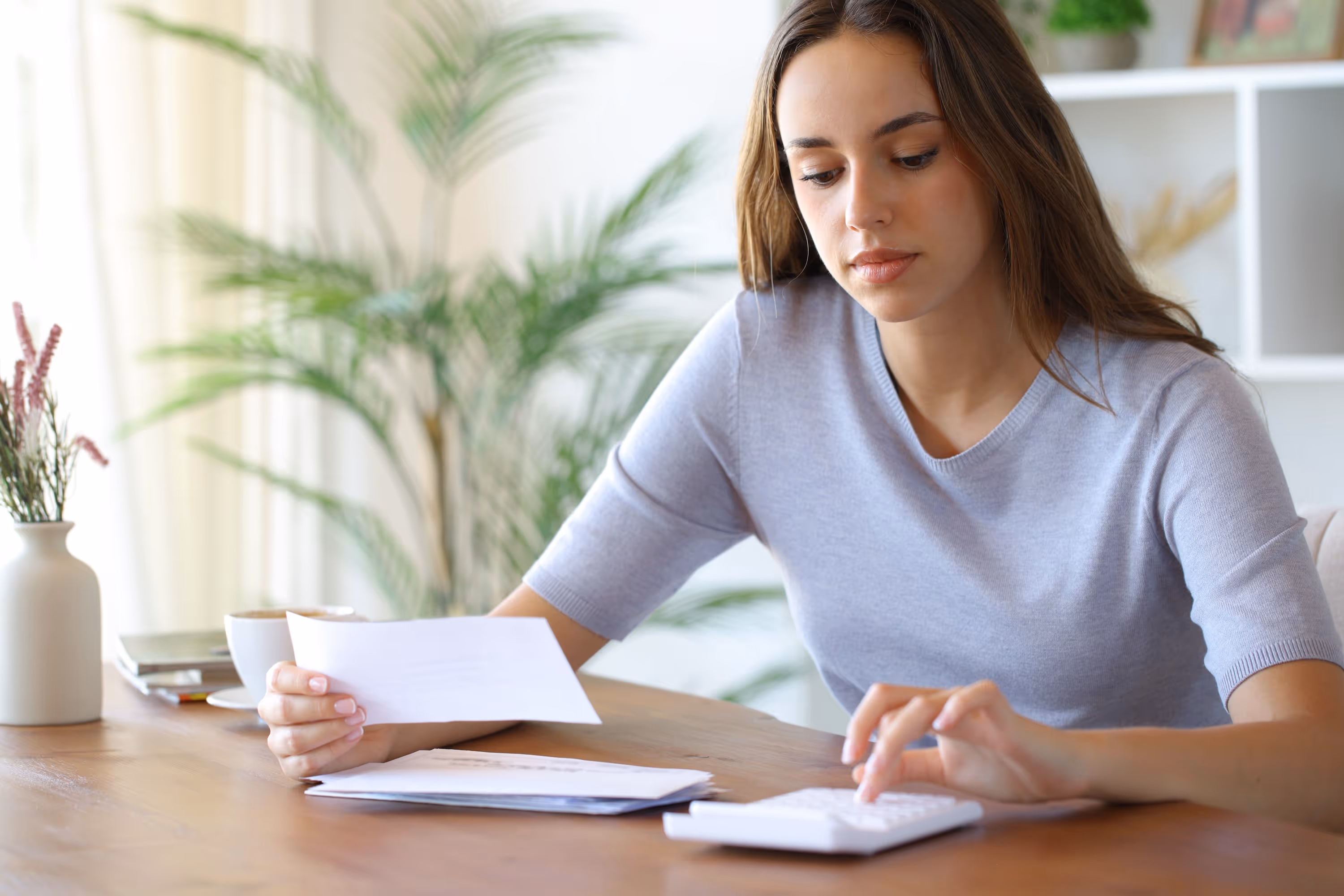 A young woman budgeting and calculating finances at a table in her apartment, representing the value and comfortable home life at Paloma in San Antonio, Texas.