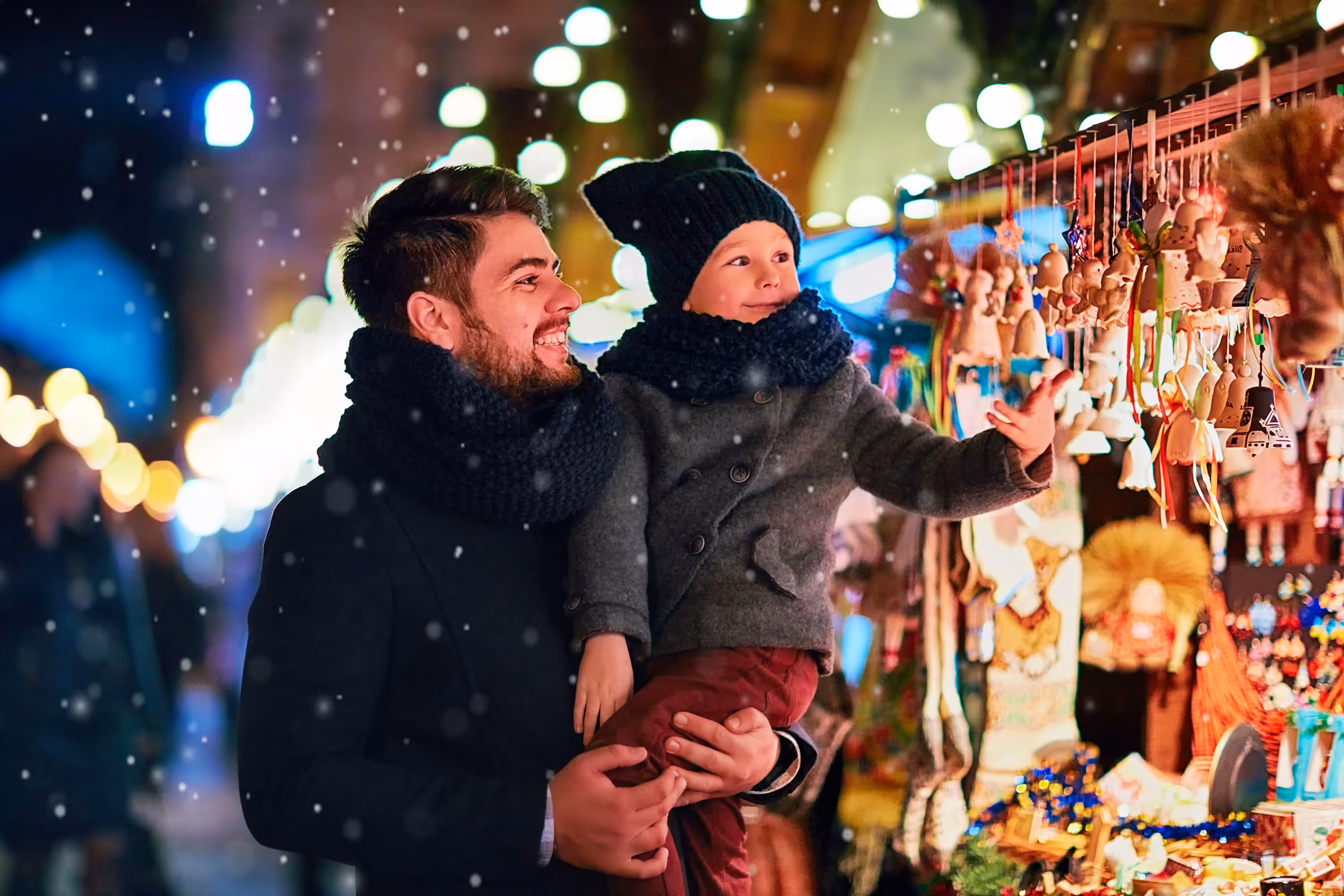 A father holding his child at a festive outdoor winter market, looking at holiday ornaments, representing the seasonal cheer and local activities near Paloma Luxury Apartments in San Antonio, TX.
