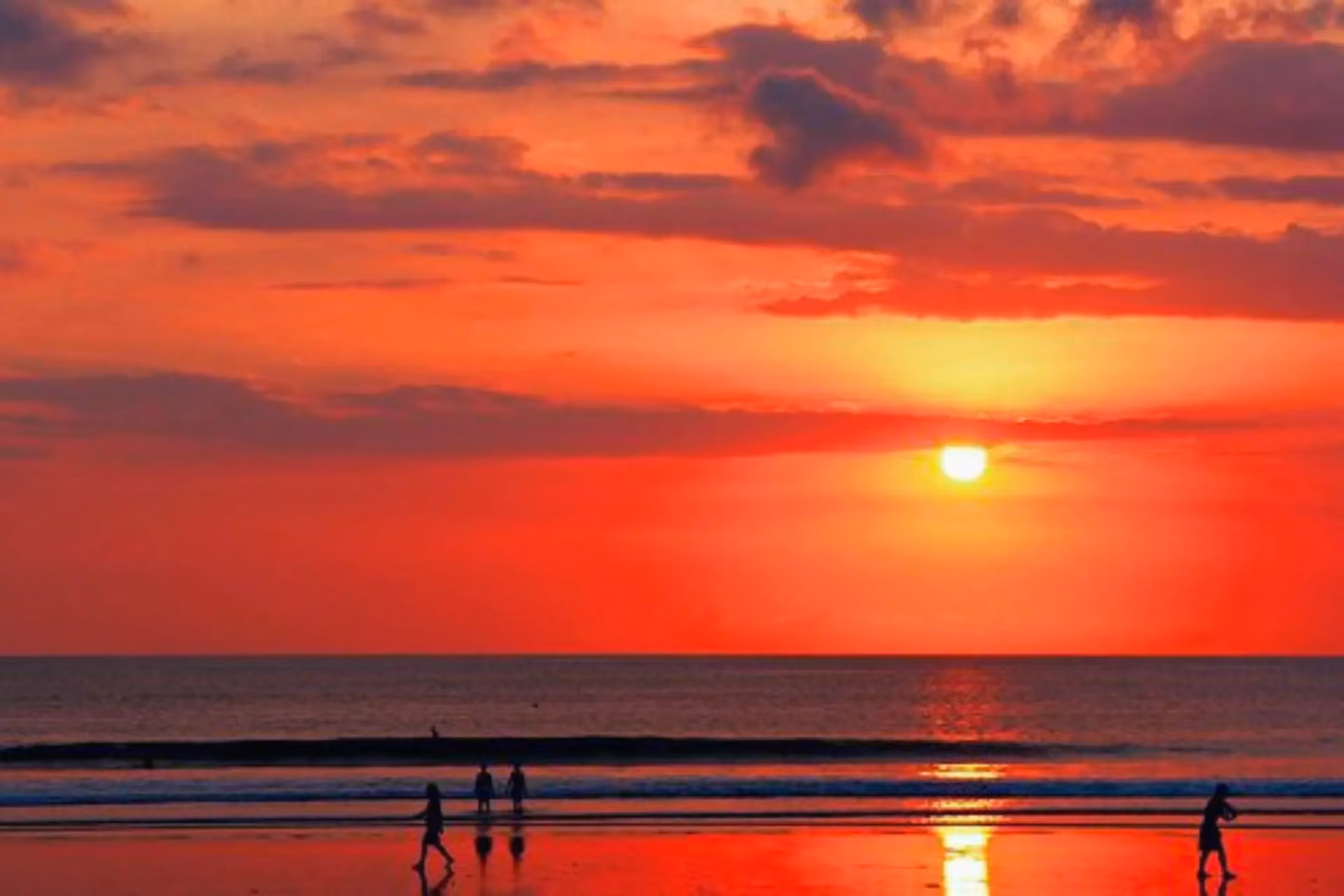 People walk by as the sun sets on Kuta beach