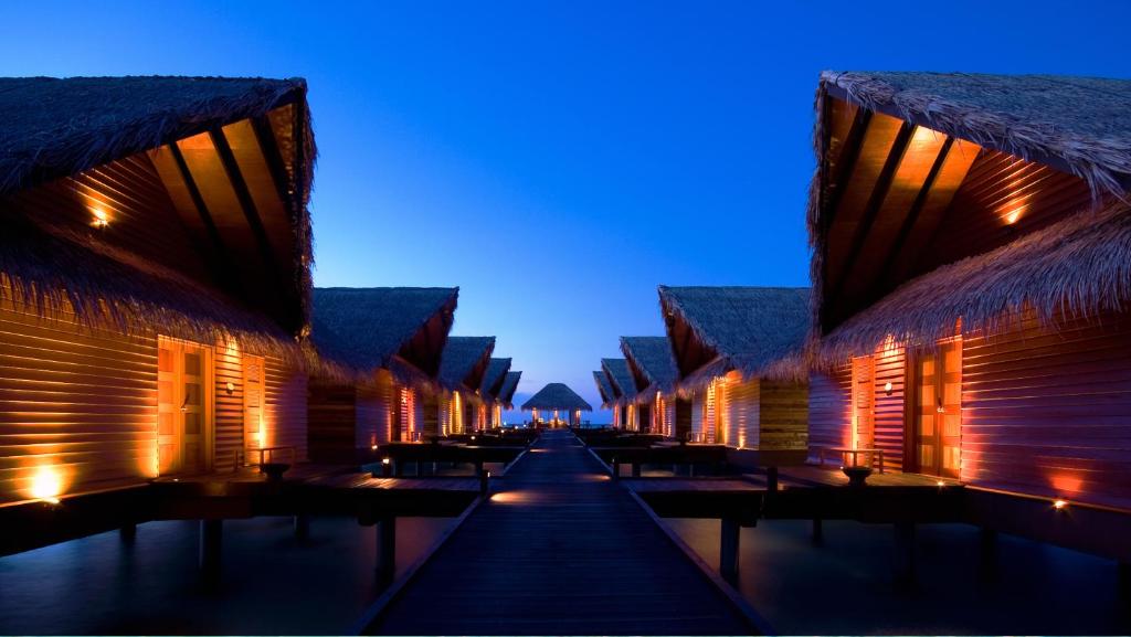 Overwater villas lit up at dusk over the ocean.
