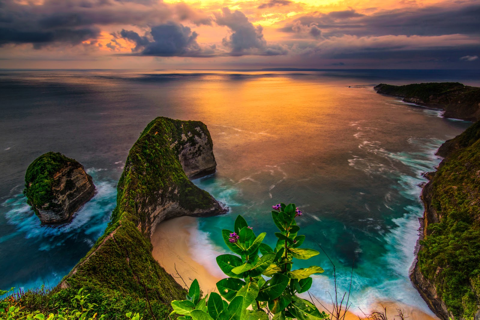 Kelingking Beach in Bali at sunset, showing steep cliffs covered in green vegetation and a sandy cove.