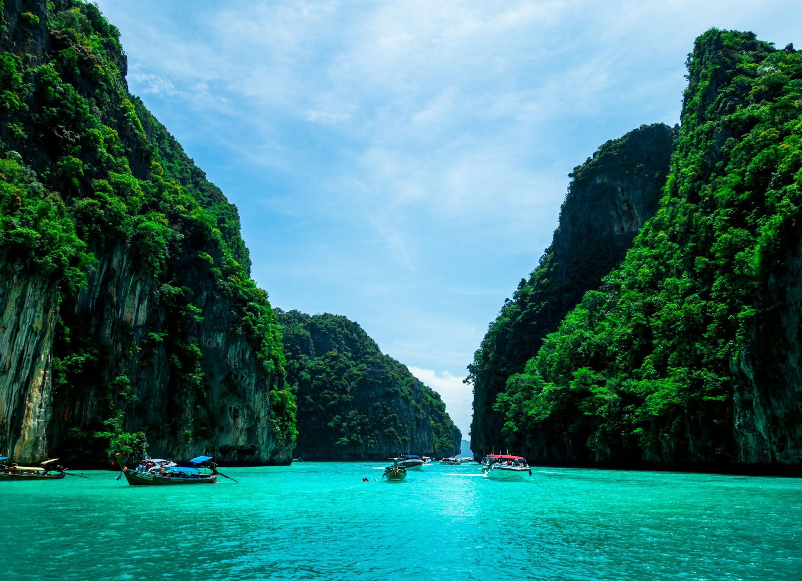 Boats floating on crystal-clear water at Phi Phi Islands in Thailand, with dramatic limestone cliffs covered in greenery.