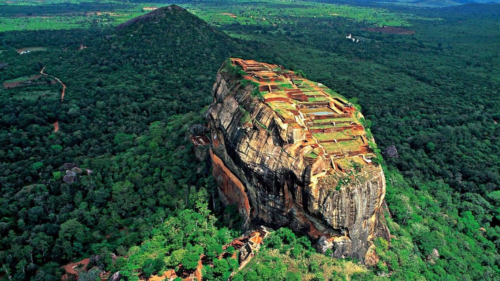 The ancient Sigiriya Rock Fortress rises surrounded by green forests in Sri Lanka.