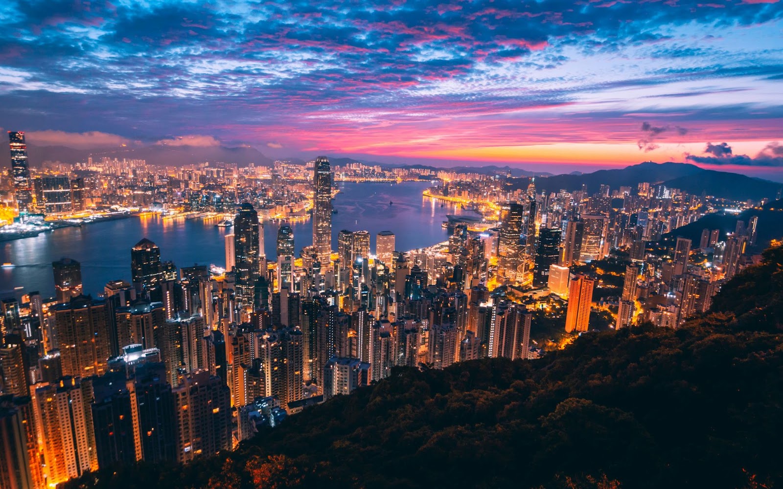 Hong Kong’s skyscrapers and Victoria Harbour under a vibrant sunset sky.