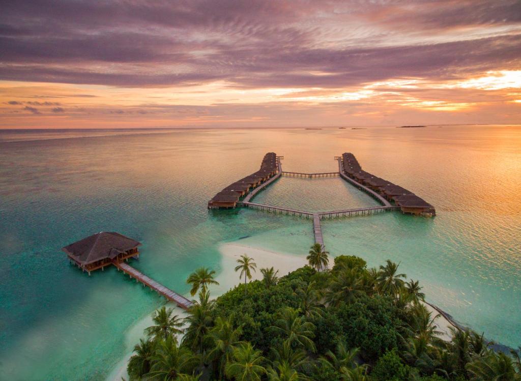 Medhufushi Island Resort in Maldives, showing water villas stretching over the ocean with a sunset.