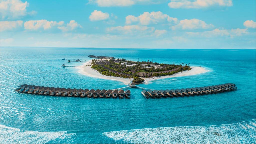 Brennia Kottefaru Maldives, showcasing long rows of overwater villas stretching into the ocean, with a lush island and sandy beaches in the background.