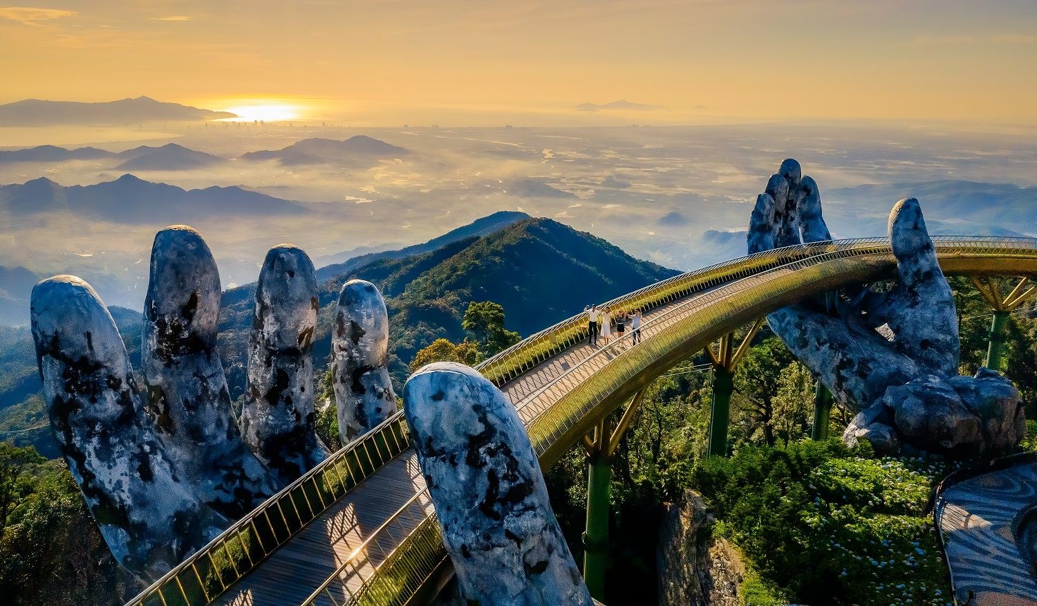 The Golden Bridge in Da Nang supported by two giant stone hands, with a stunning view of mountains and a sunrise.