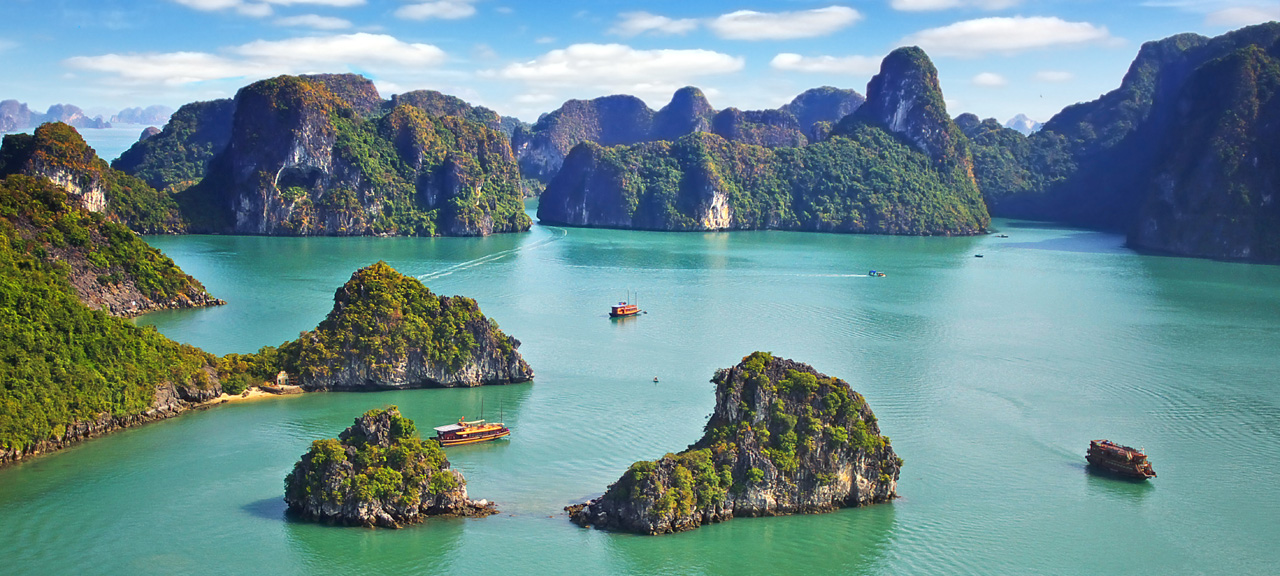 A breathtaking view of Halong Bay, with ocean, limestone cliffs, and boats sailing between lush islands.