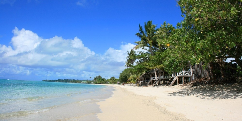 An Bang Beach in Vietnam with white sand, clear blue sea, palm trees, and wooden beach huts along the shore.
