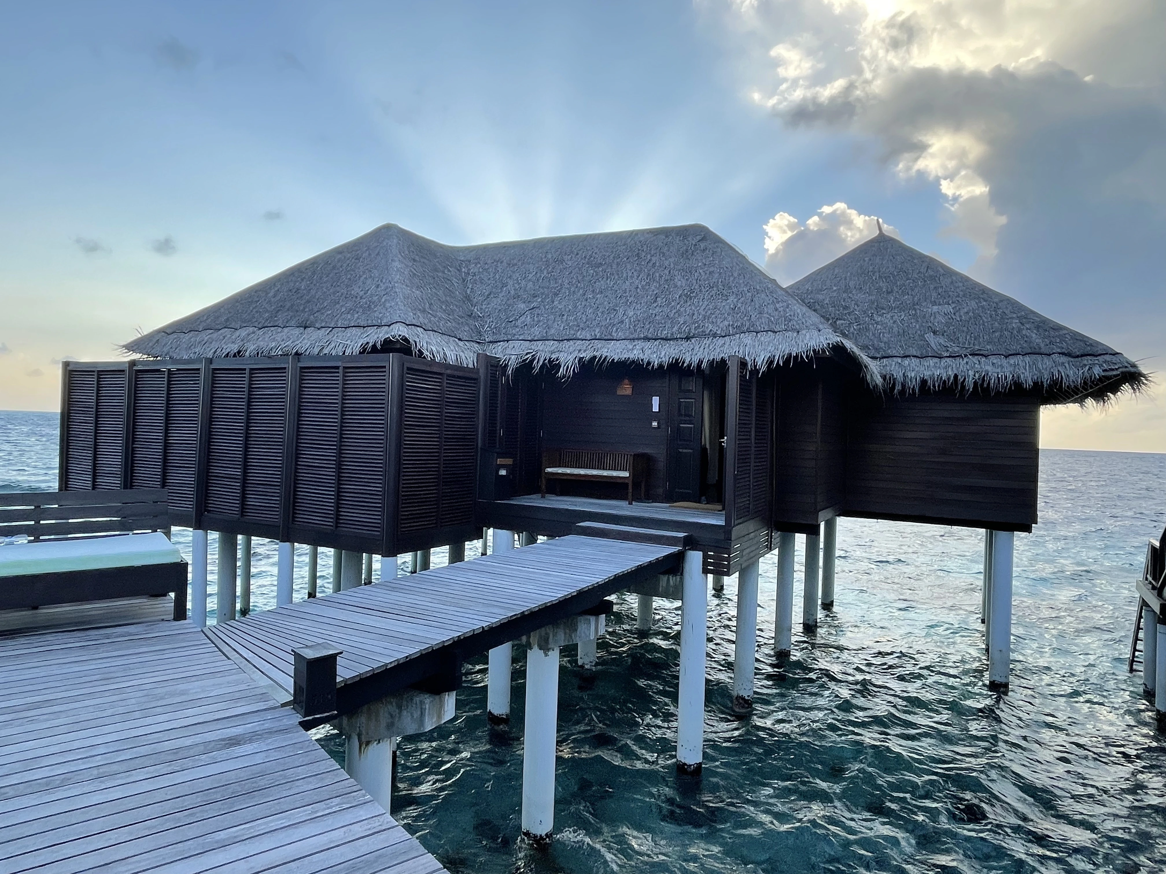 Overwater villas and thatched-roof huts on blue lagoon in Fiji, with palm trees and a wooden walkway stretching over the sea.