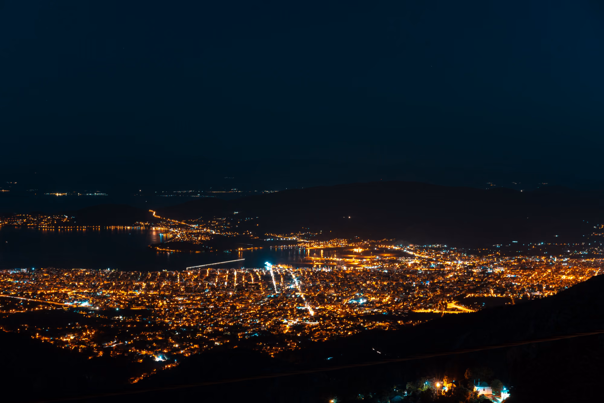 Tehran city at night showing glowing highways, countless city lights, and the Milad Tower standing under a full moon light.
