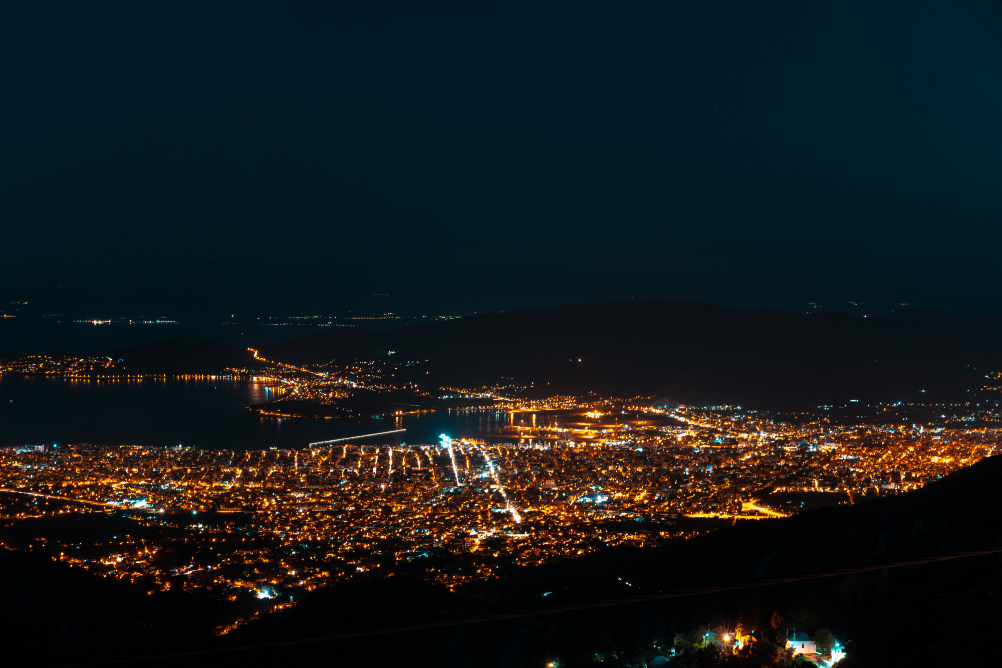 Tehran city at night showing glowing highways, countless city lights, and the Milad Tower standing under a full moon light.