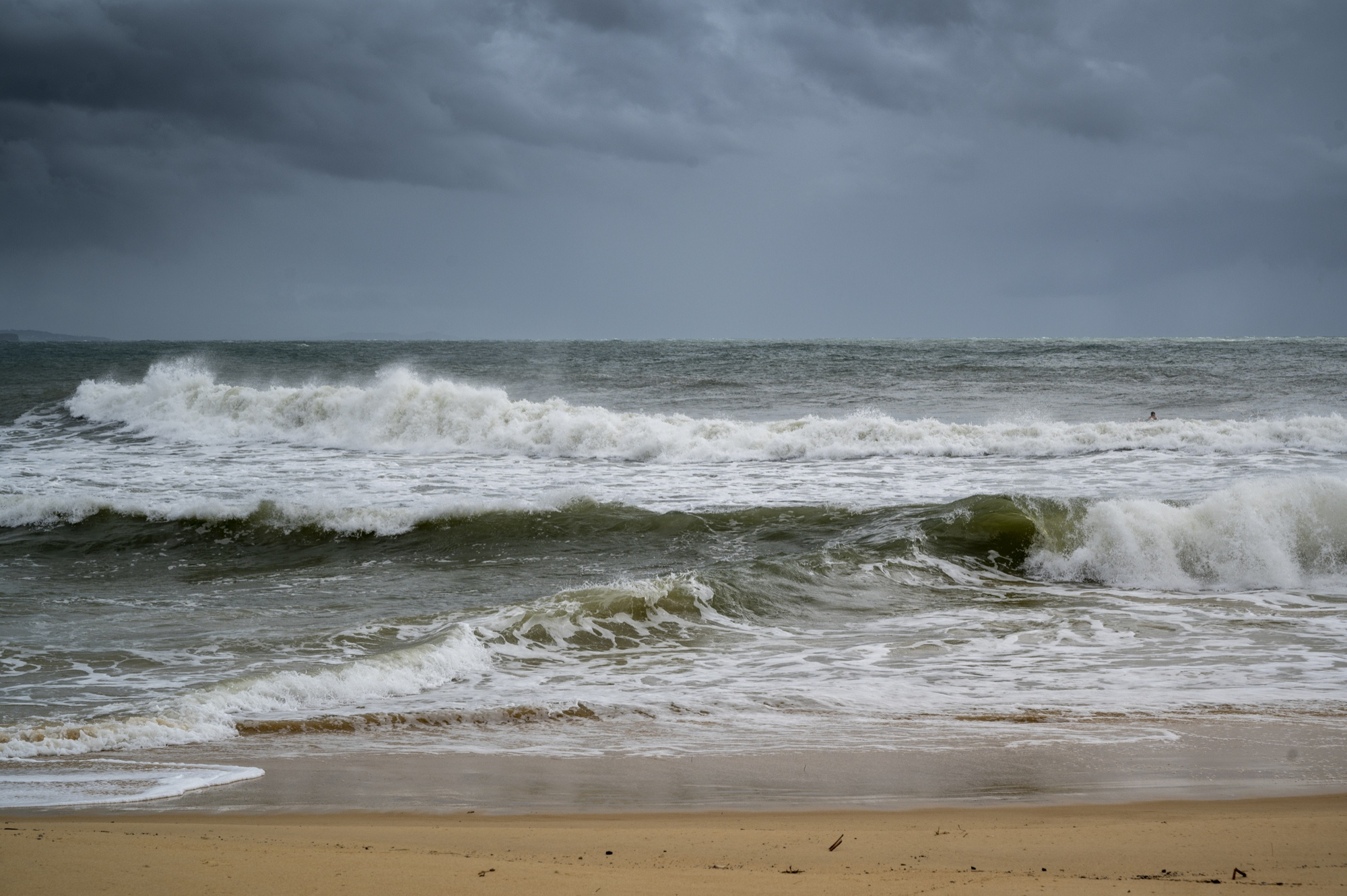 Strong waves rolling onto Karon Beach in Phuket under a cloudy and stormy sky during the rainy season.