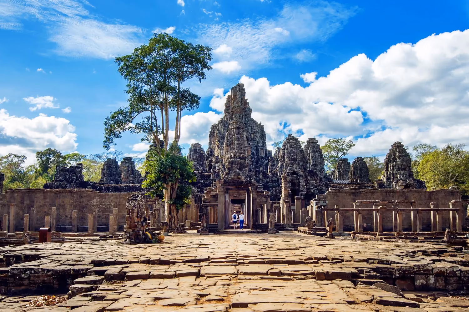 View of Angkor Wat temple in Cambodia, with visitors walking on the stone path lined by palm trees.