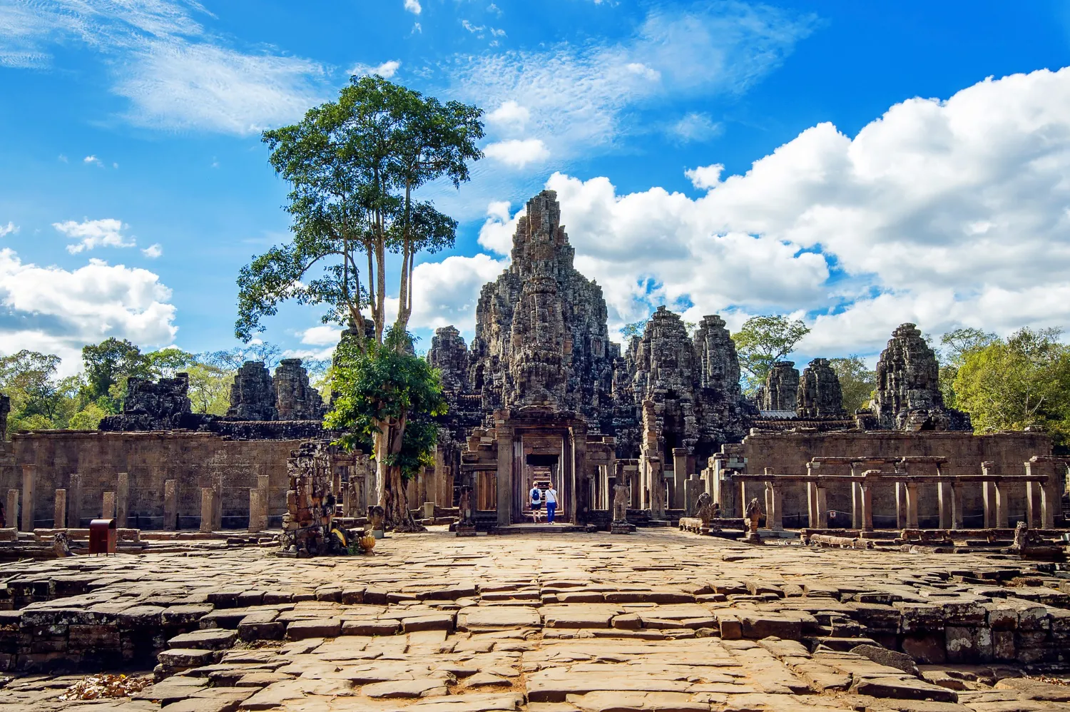 View of Angkor Wat temple in Cambodia, with visitors walking on the stone path lined by palm trees.