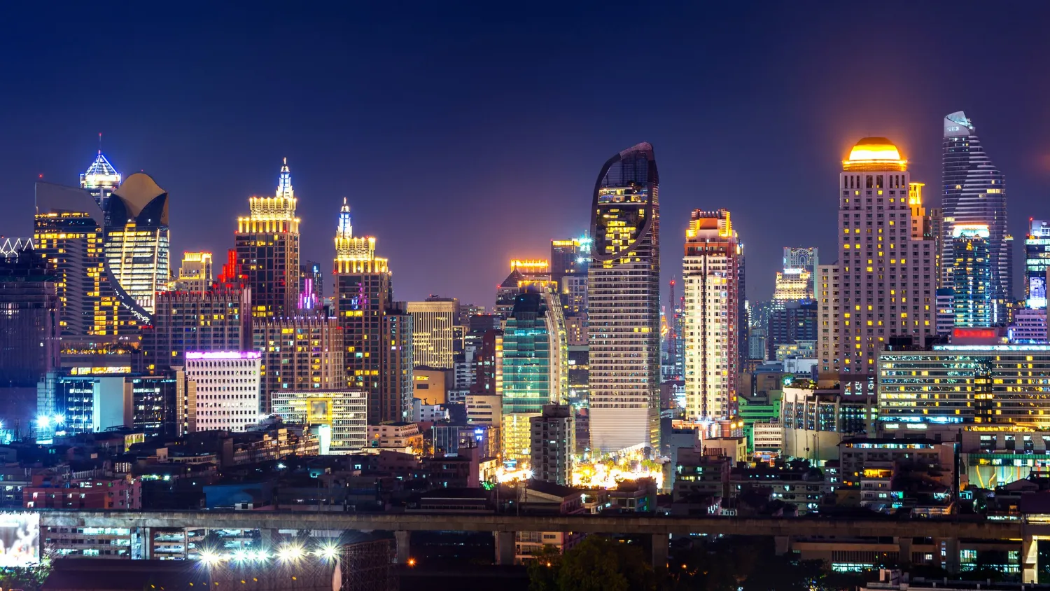 Skyline of Thailand with modern skyscrapers and a river at night.