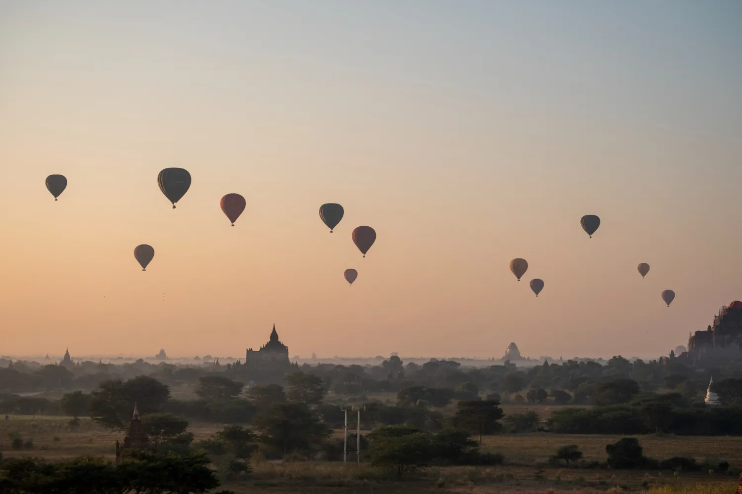 Sunrise over the plains of Bagan, Myanmar, showing dozens of ancient Buddhist temples and pagodas, with hot air balloons floating.