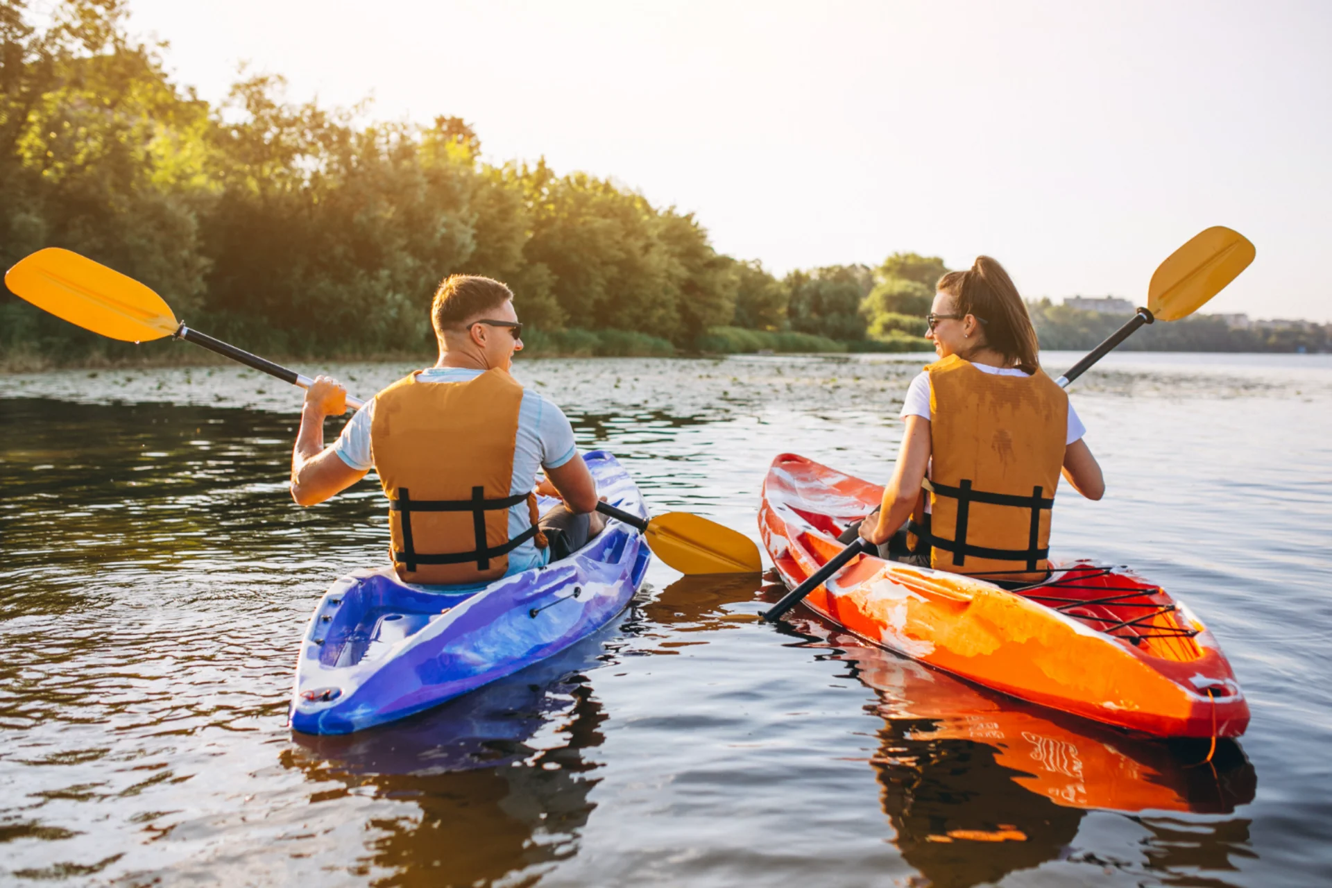 Couple kayaking on scenic river surrounded by green trees in Thailand, highlighting adventure water sports activities in Thailand vs UAE activity compariso