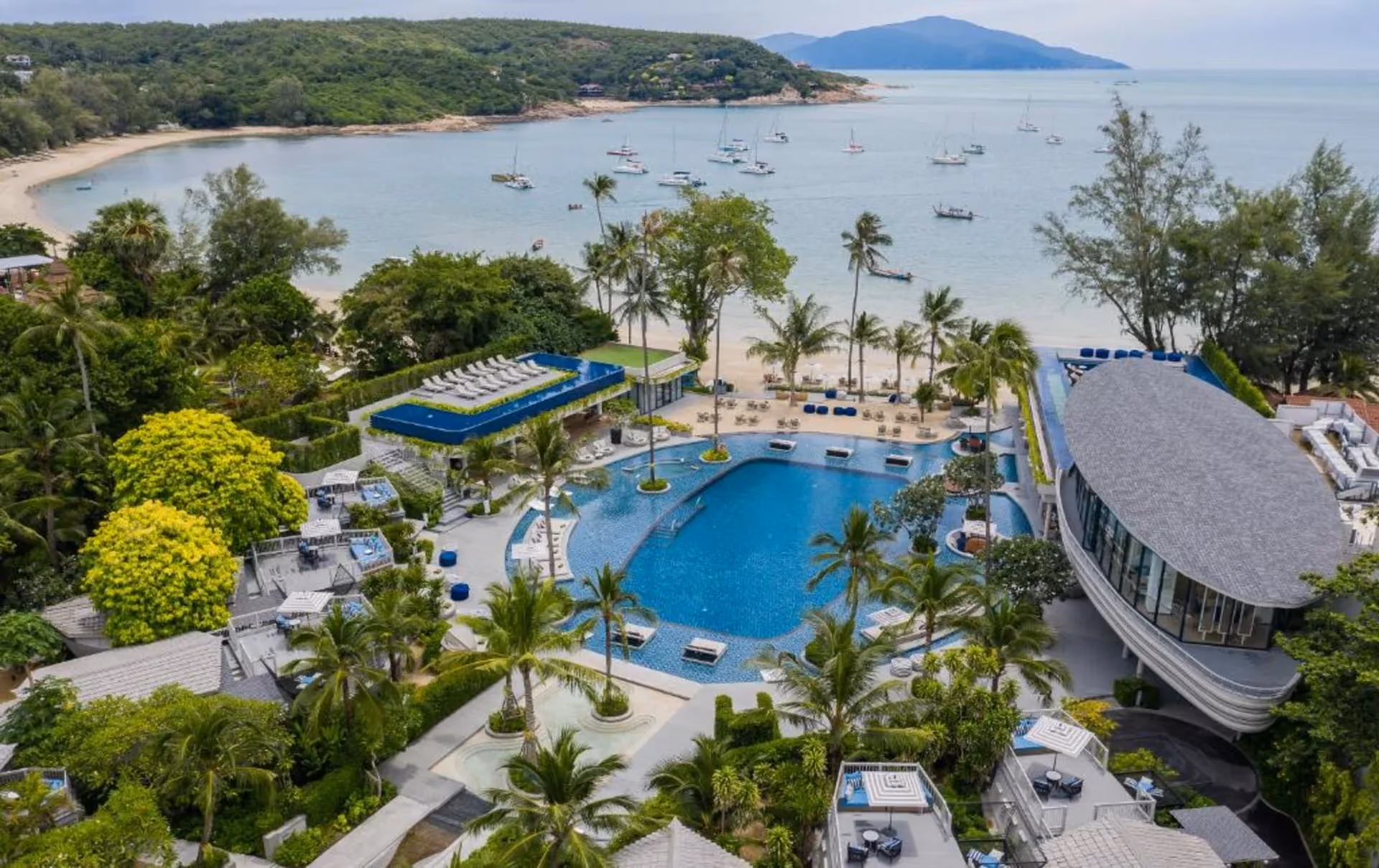 Melia Koh Samui showcases Thailand's signature luxury scale — a sweeping resort pool, manicured gardens, direct beach access, and a bay dotted with sailboats, all in one panoramic view.