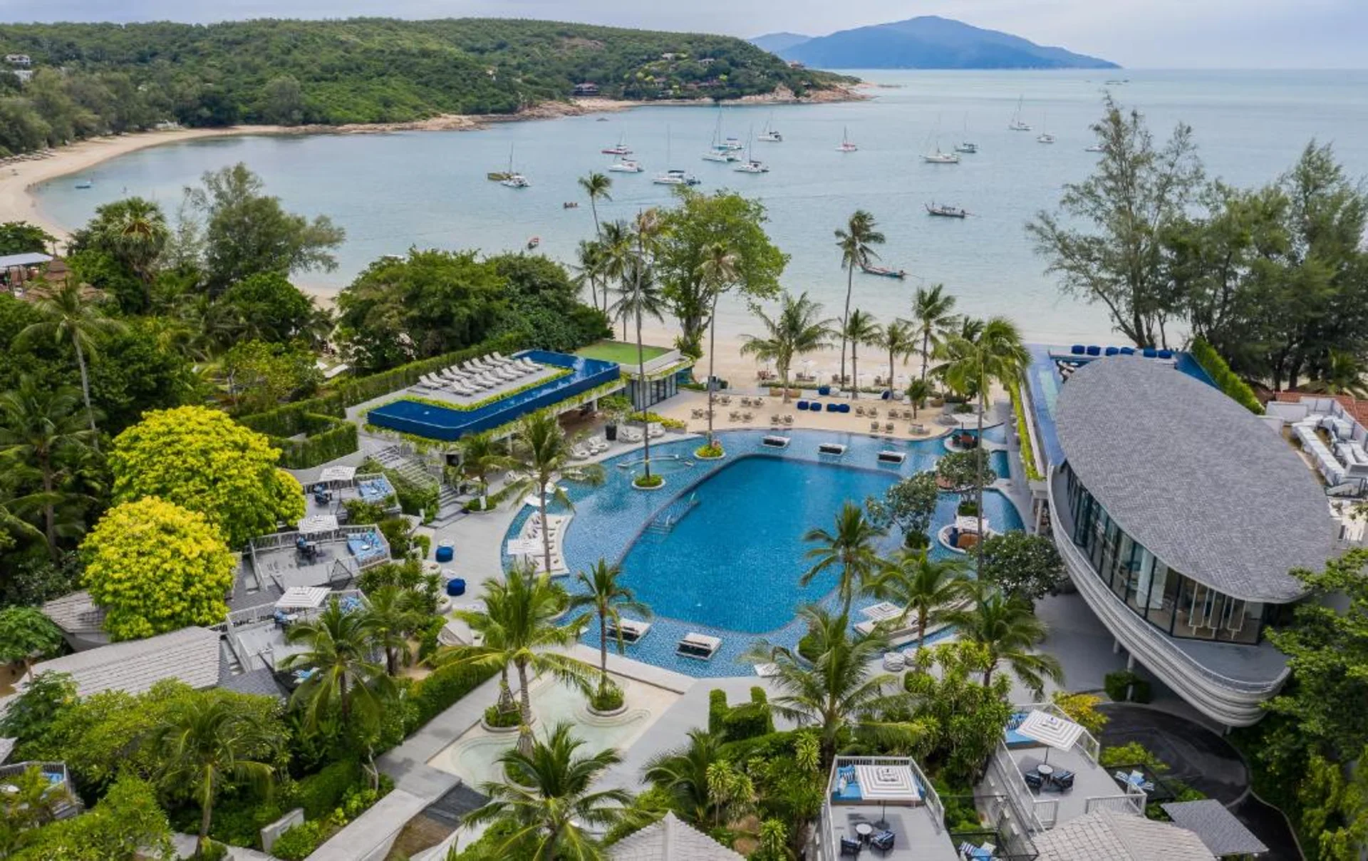Melia Koh Samui showcases Thailand's signature luxury scale — a sweeping resort pool, manicured gardens, direct beach access, and a bay dotted with sailboats, all in one panoramic view.