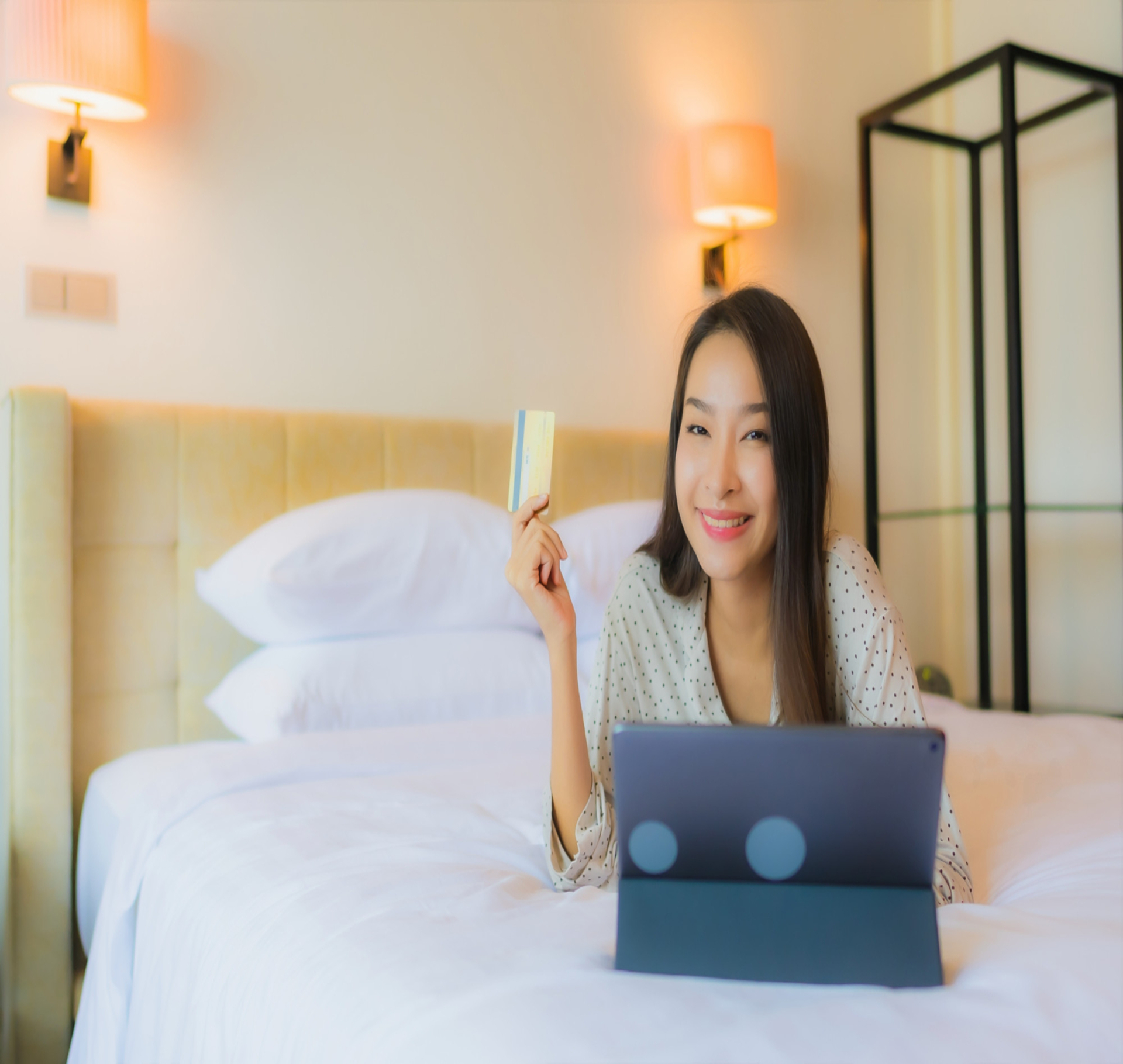 Woman on hotel bed holding credit card with tablet — budget stays Georgia vs Azerbaijan trip