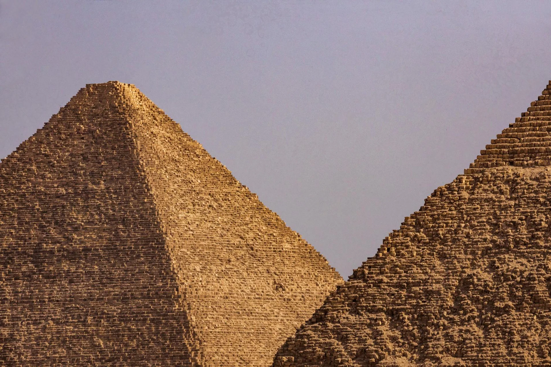 Two Egyptian pyramids photographed up close against a clear blue sky
