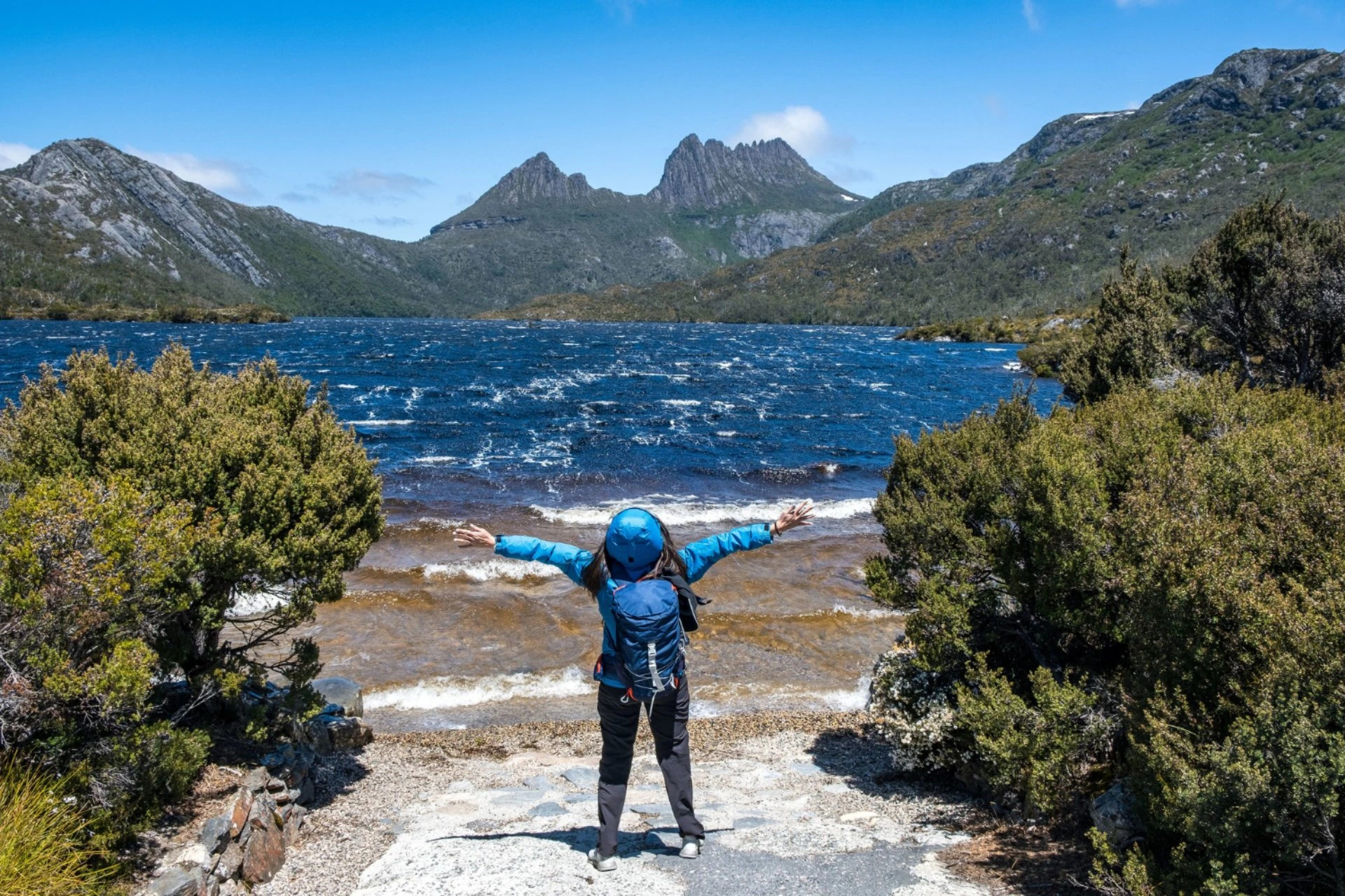 Traveler standing beside a peaceful mountain lake, reflecting the open landscapes and low crowd experience in New Zealand vs Switzerland