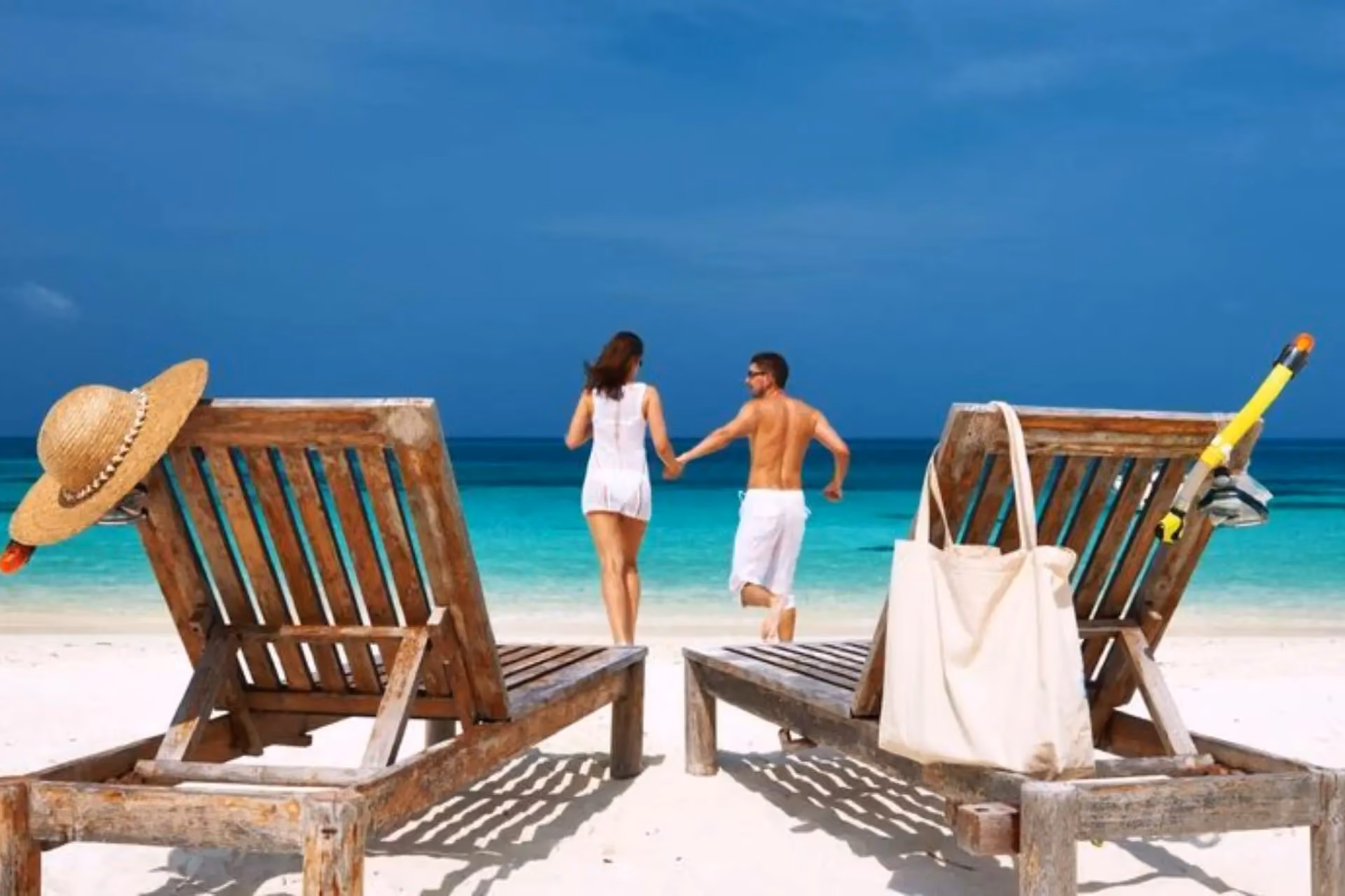 Couple holding hands on Mauritius beach near wooden chairs