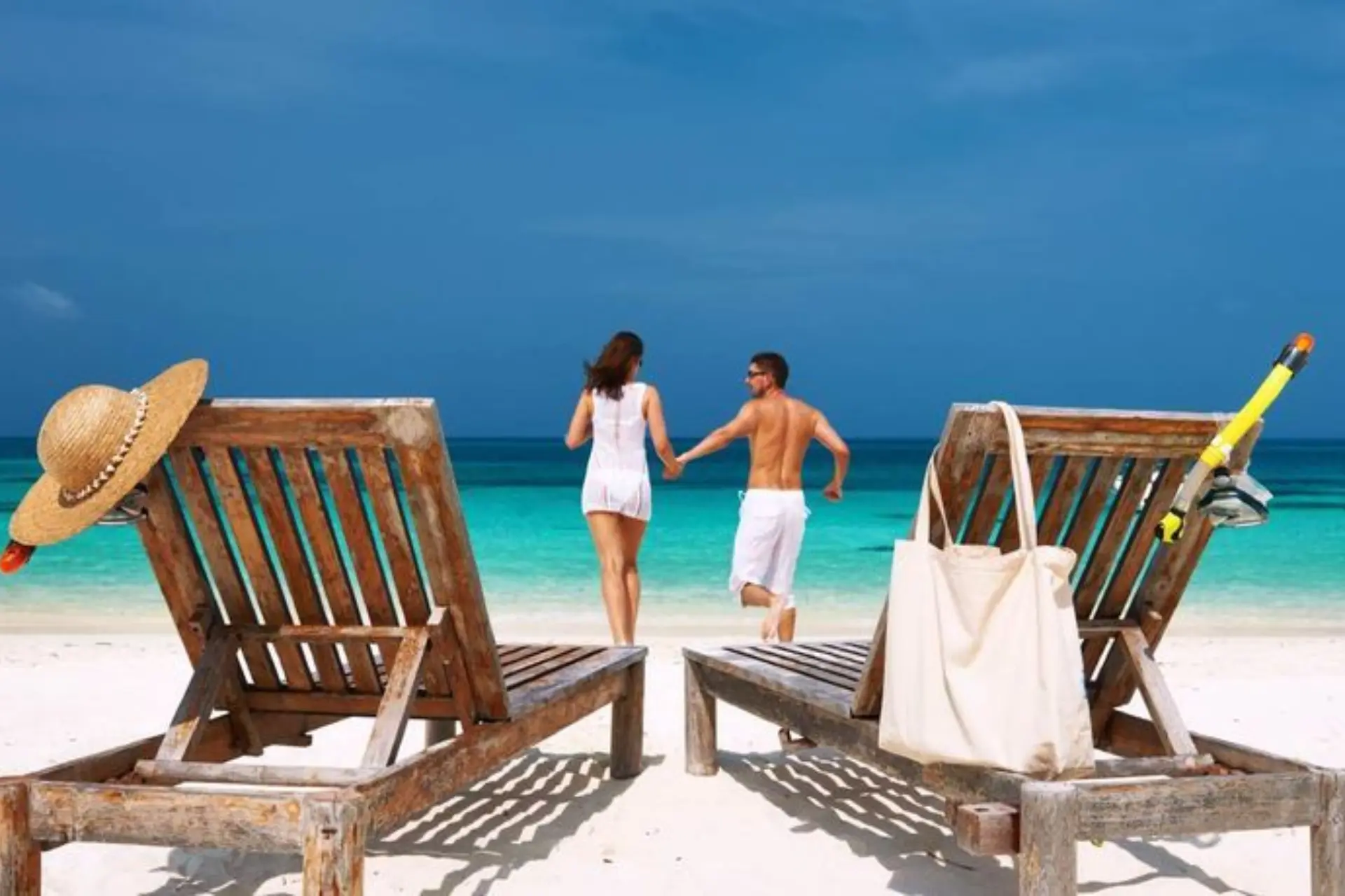 Couple holding hands on Mauritius beach near wooden chairs
