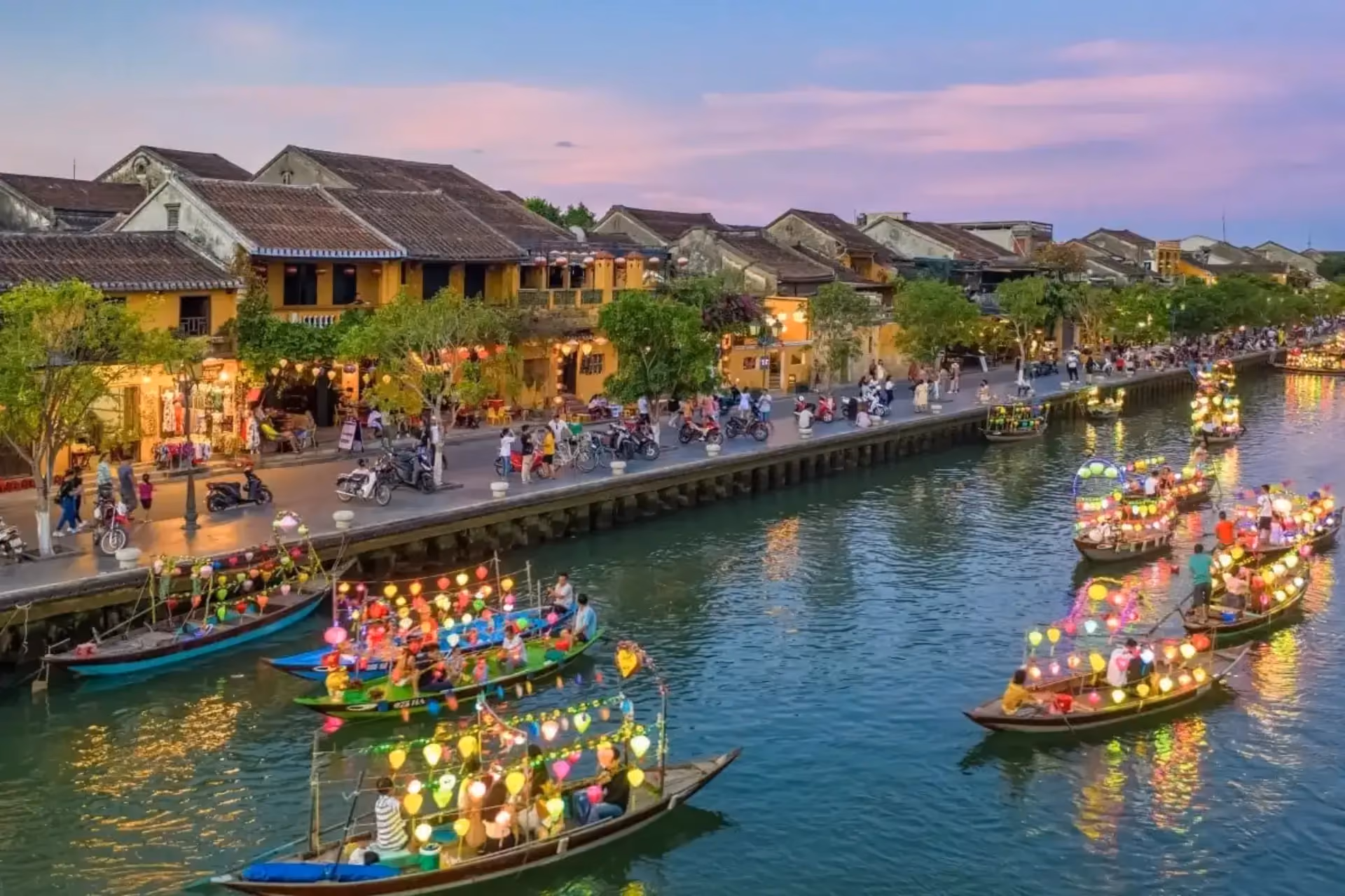 Colorful boats on Thu Bon River at dusk with yellow buildings