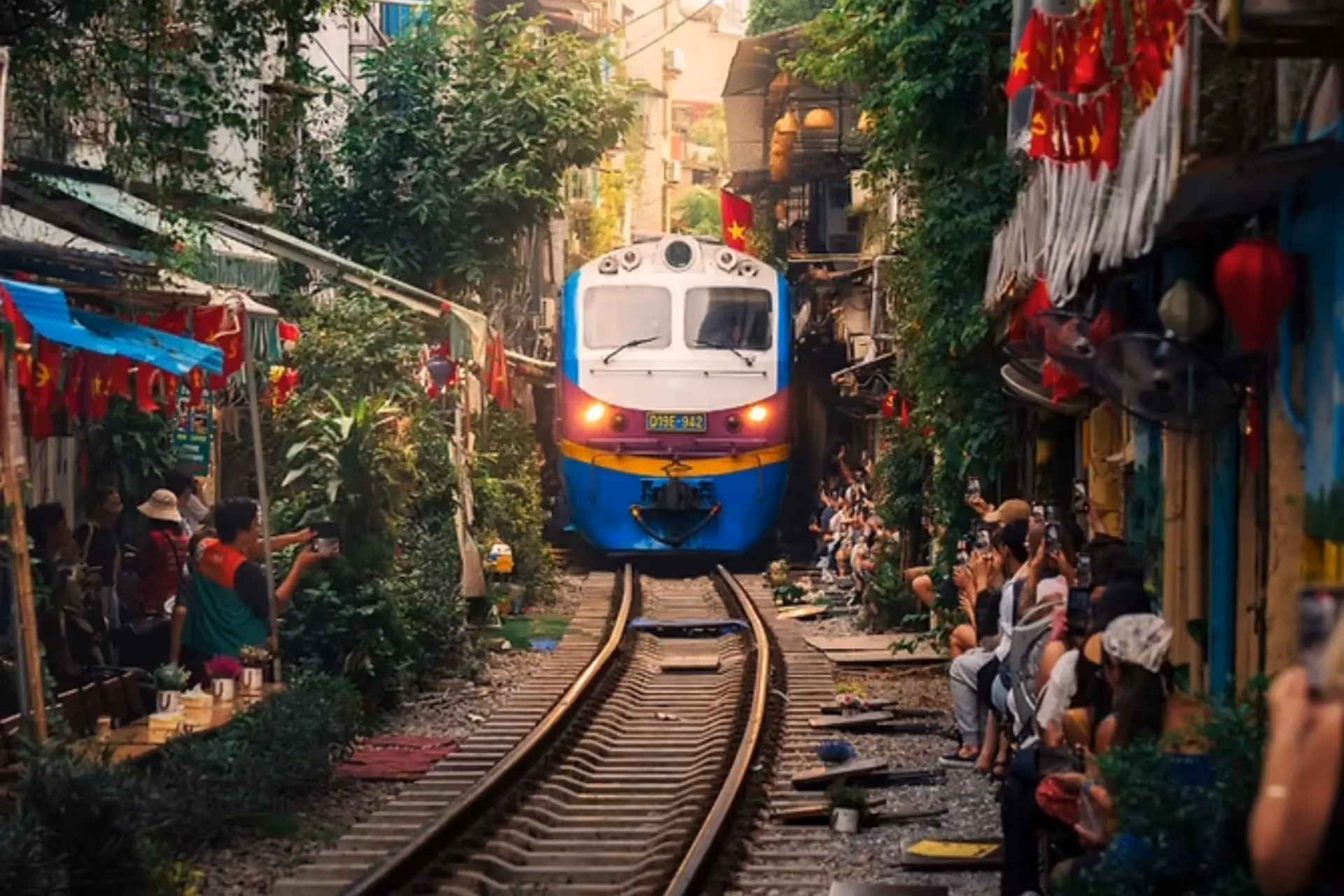 Train approaching through narrow Hanoi street lined with shops and people