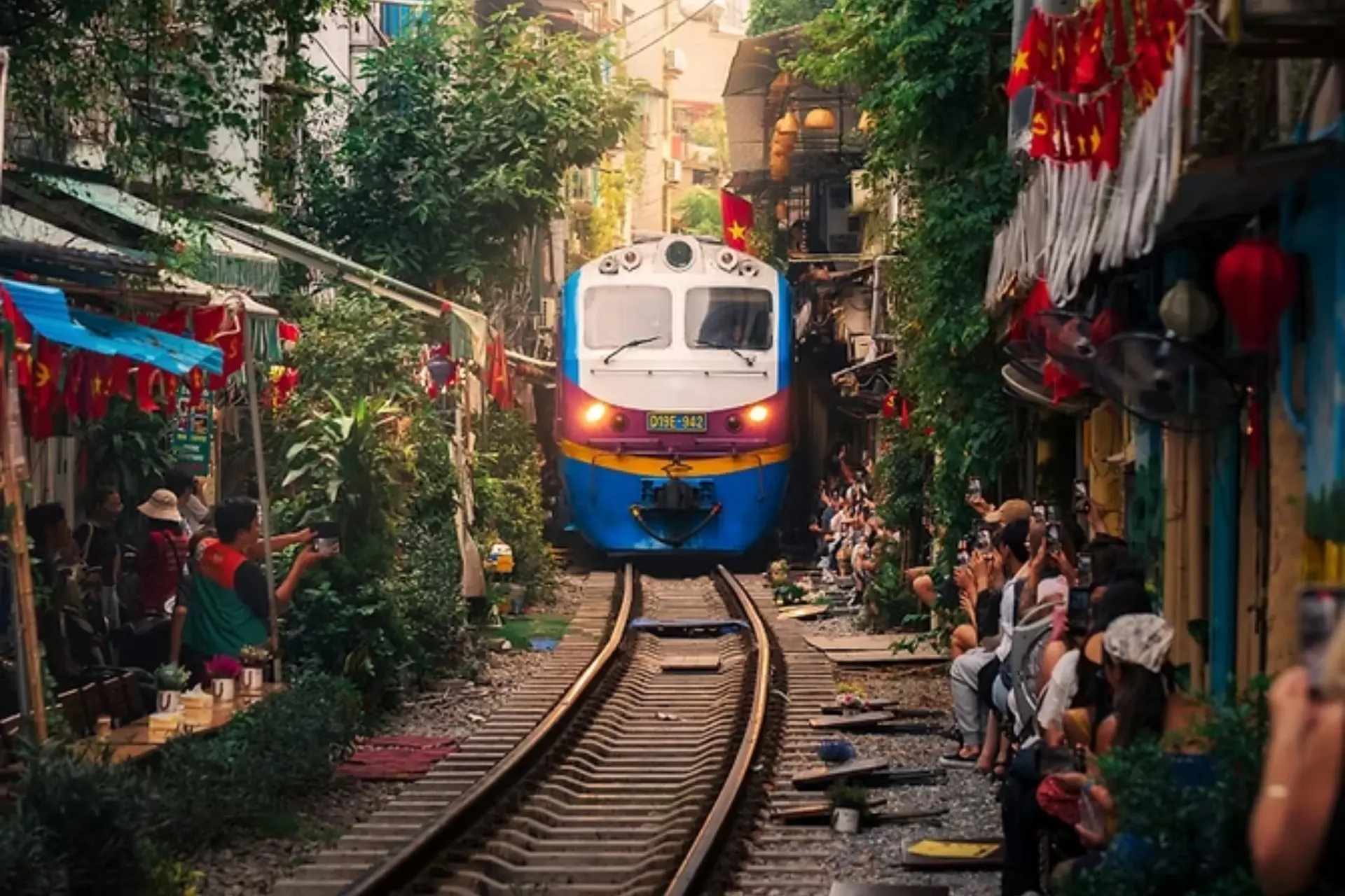 Train approaching through narrow Hanoi street lined with shops and people