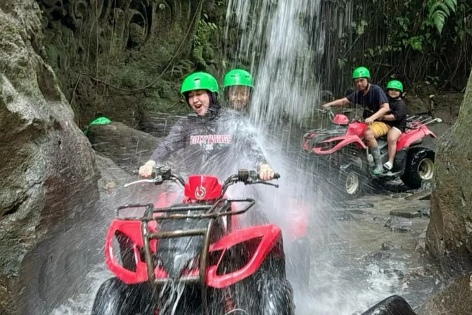 People riding red ATVs through waterfall in Ubud jungle