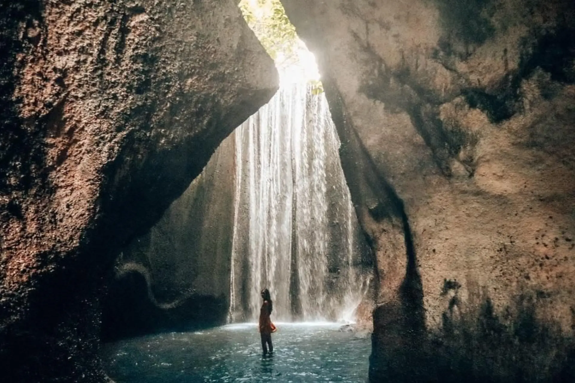 Person standing in water under Tukad Capung waterfall in Bali