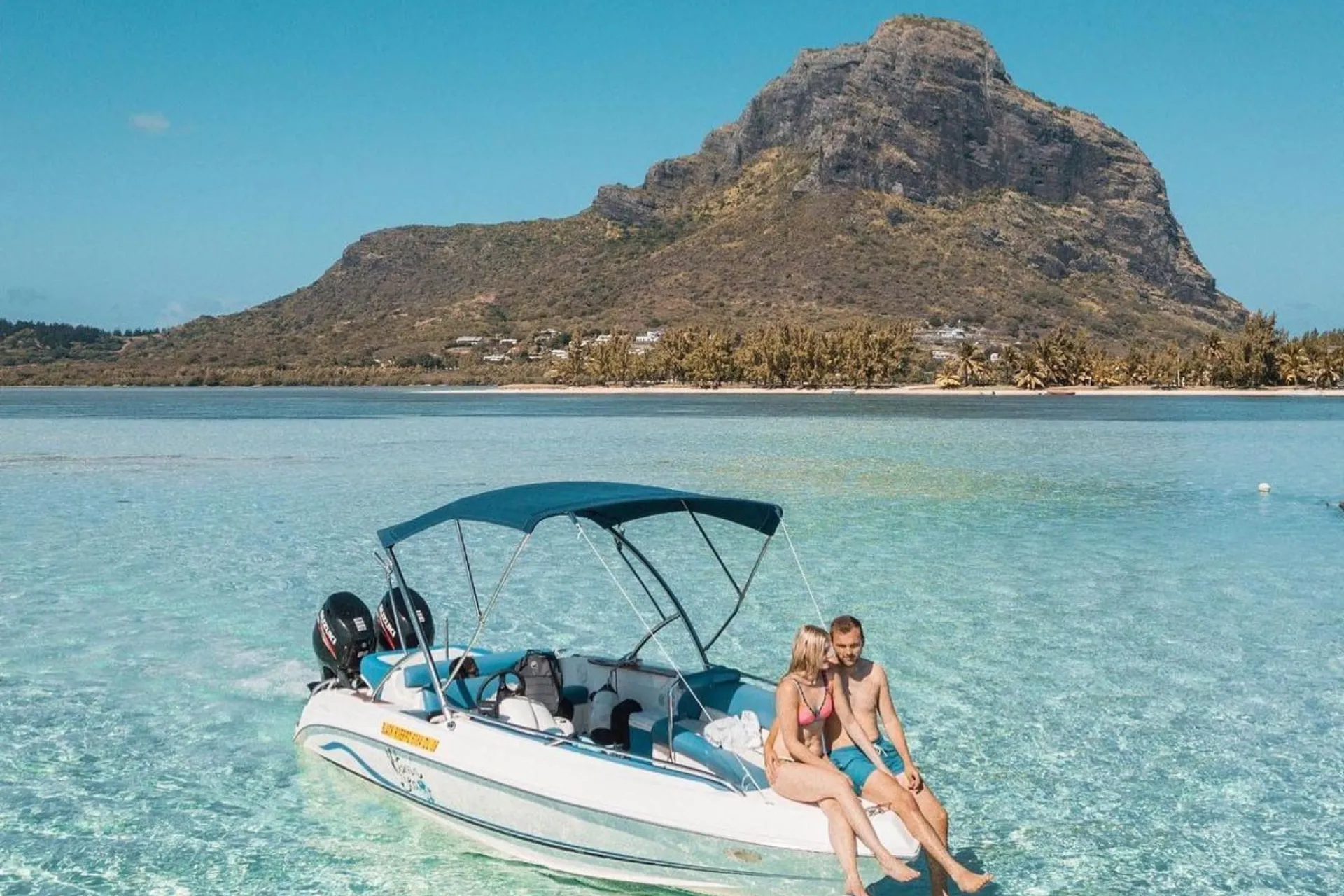 Couple sitting on boat in clear water, Mauritius mountain behind