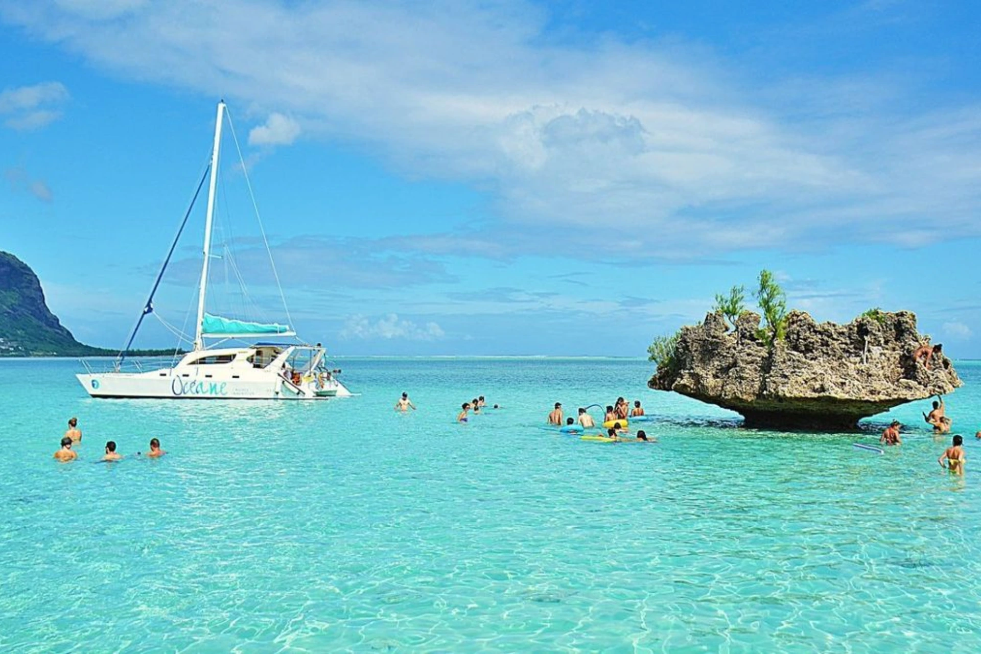 Catamaran sailboat with swimmers in clear blue water near rock island, Mauritius